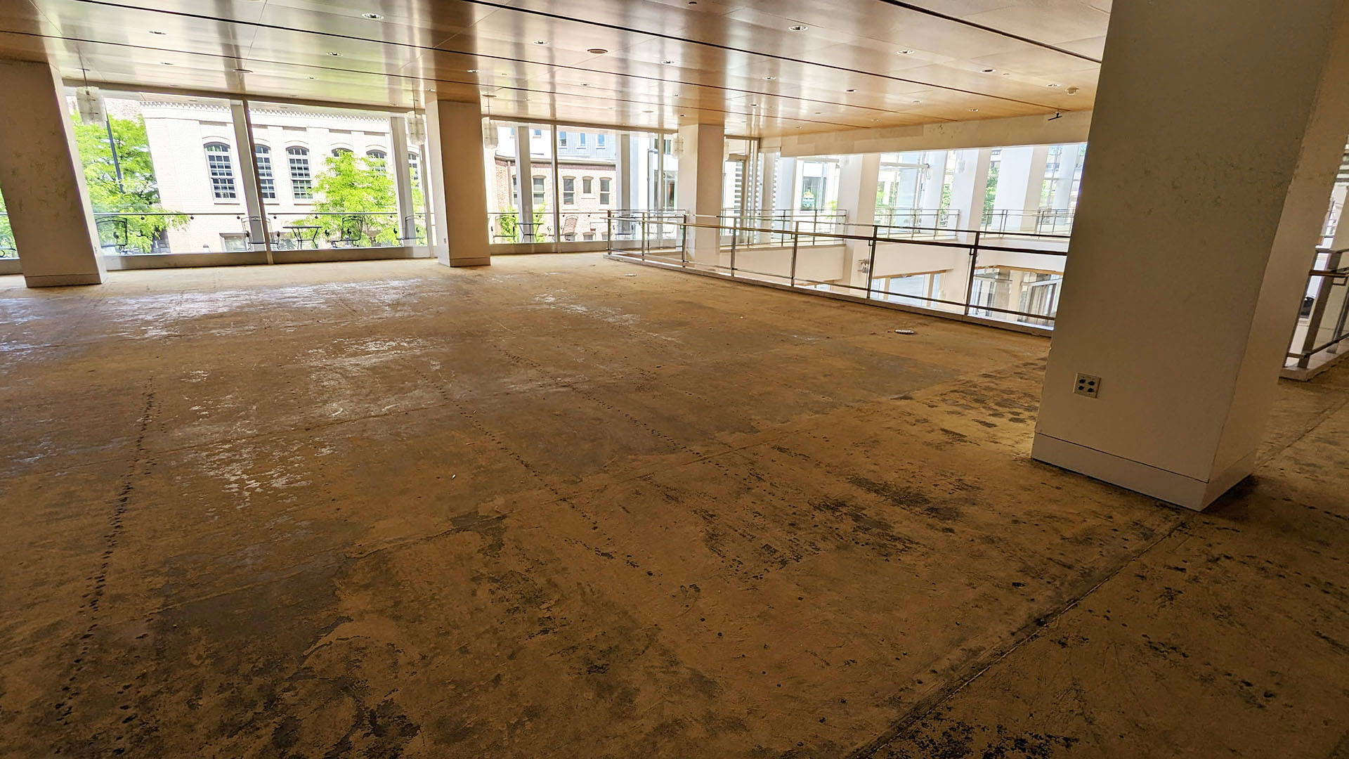 Tan floor that has been stripped of carpet with glass windows in the back