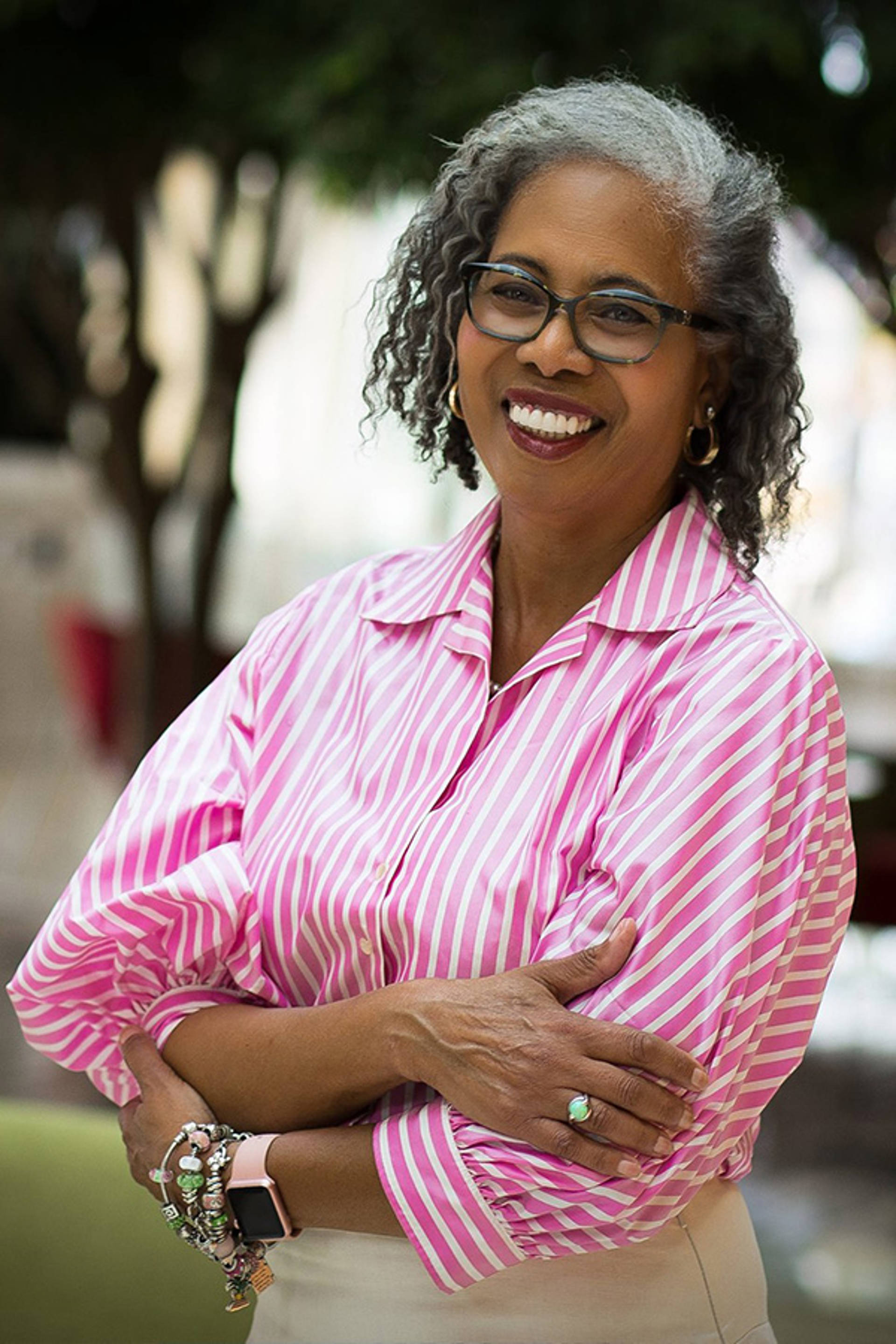 A headshot of a smiling middleaged African American woman with medium length hair, glasses and a pink button up shirt.