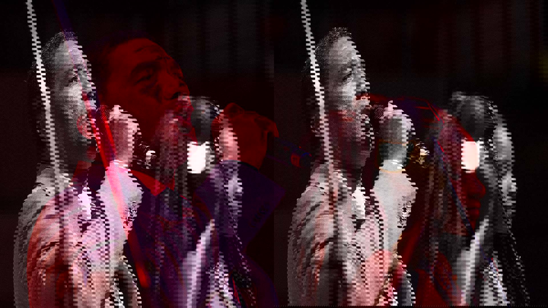 A man with short dark hair and a suit is singing into a microphone.