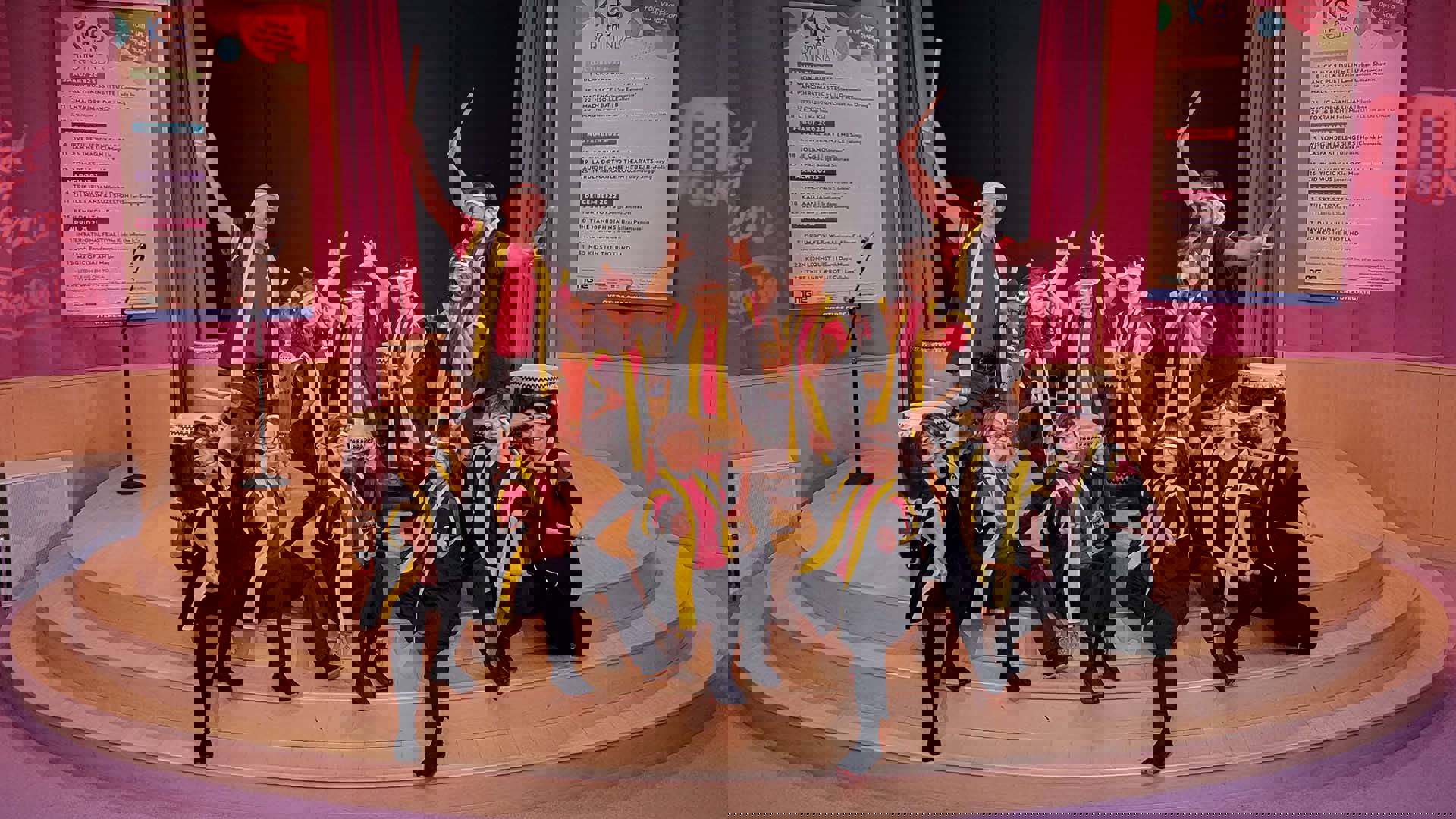 A group of 12 people in red shirts, black pants, white headbands and yellow and black vests holding wooden mallets posing to the camera.