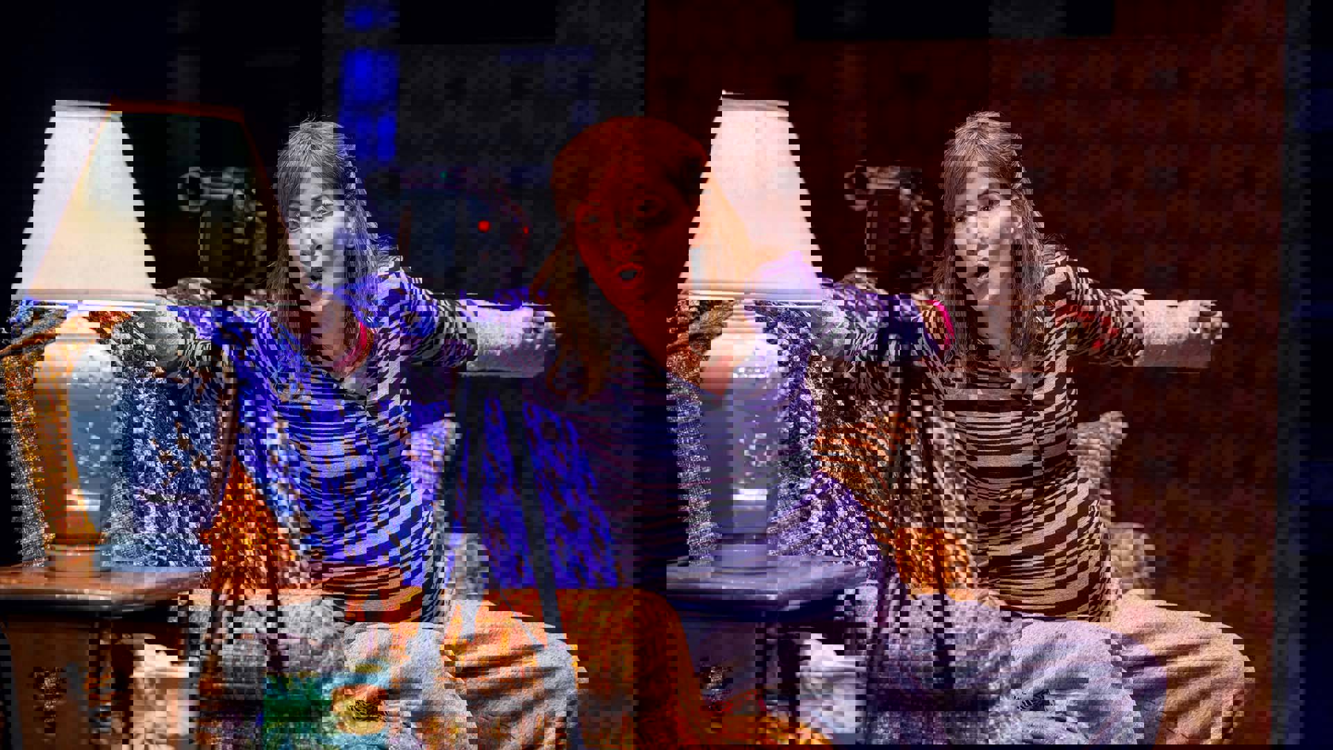 A woman with red hair and light complexion sits on a couch and speaks into a video camera.