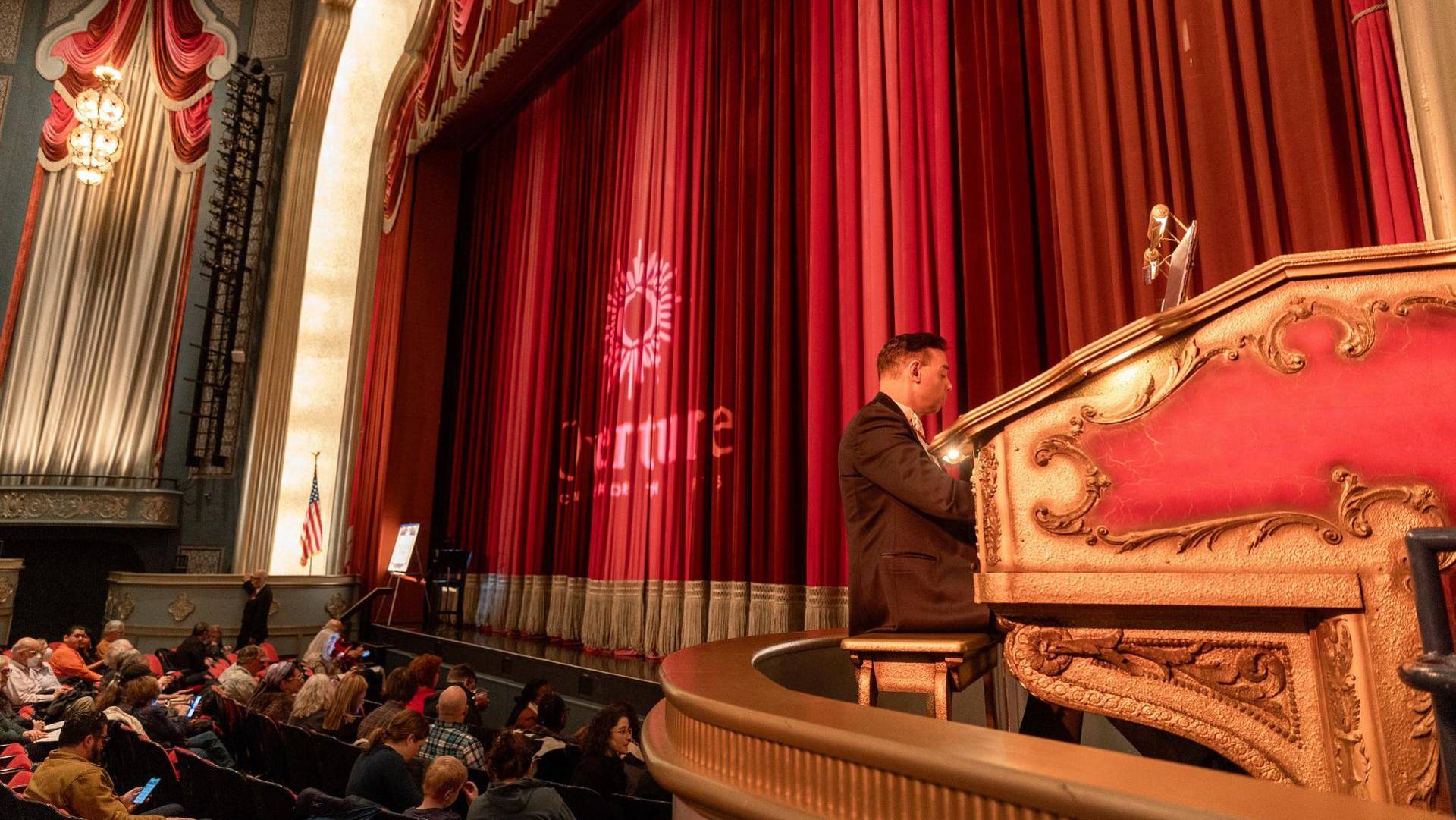 An organist at a console and the large capitol theater curtain.