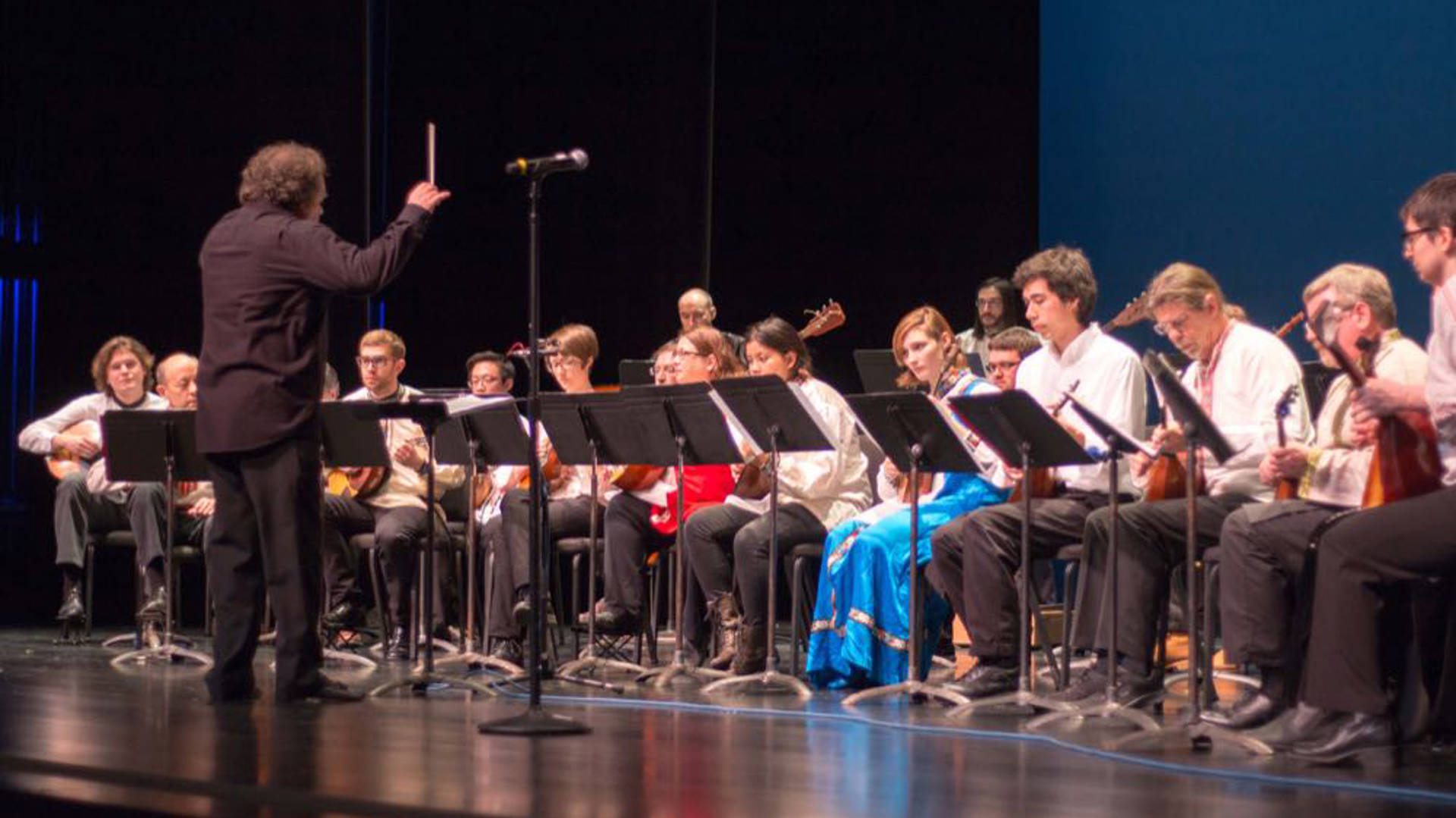 A russian folk orchestra rehearsing in a line on a dark stage.