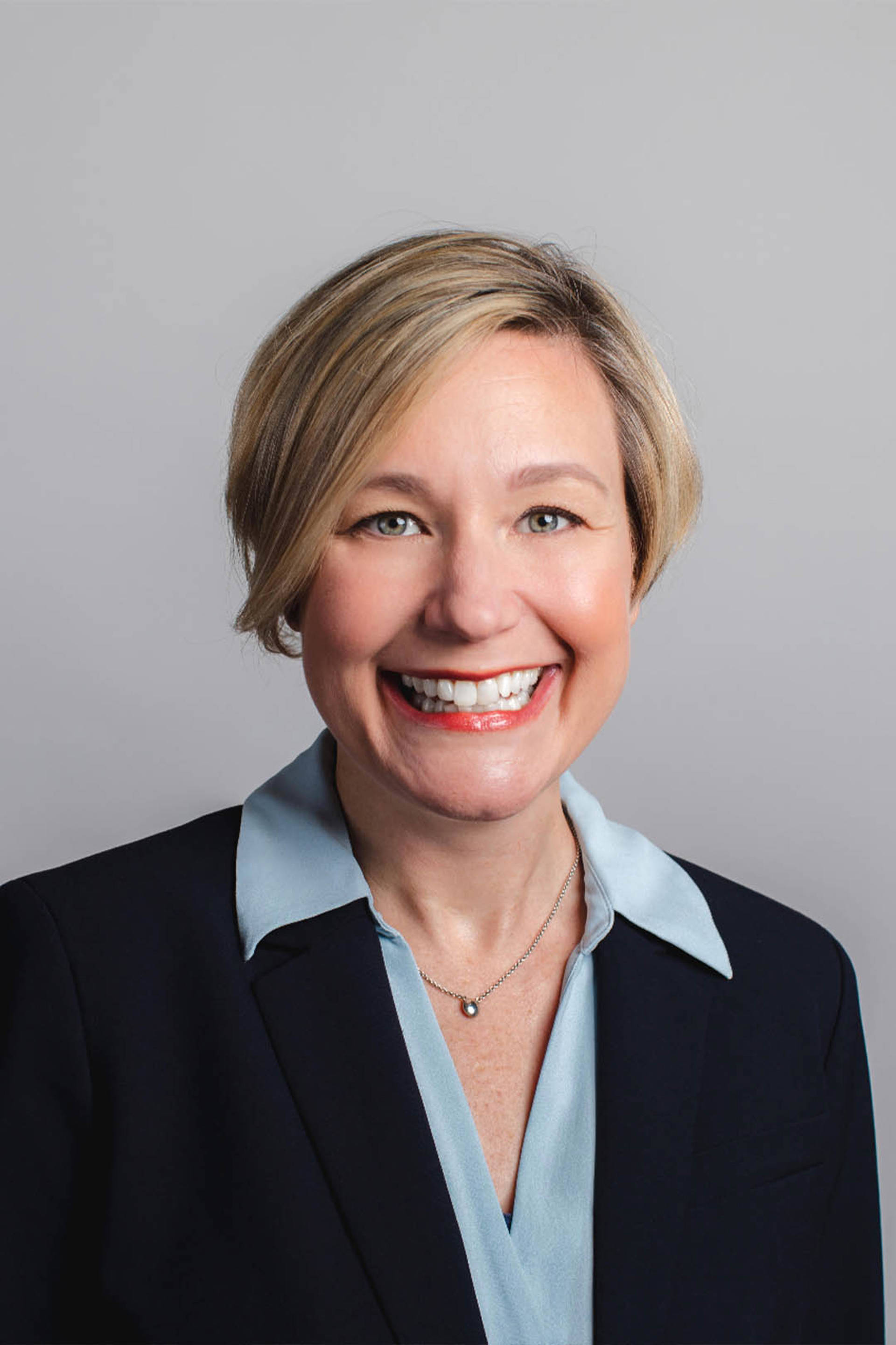Headshot of Jenie Dahlmann. She is a white woman with short, blonde hair and light, hazel eyes. She is wearing a dark jacket over a blue shirt.