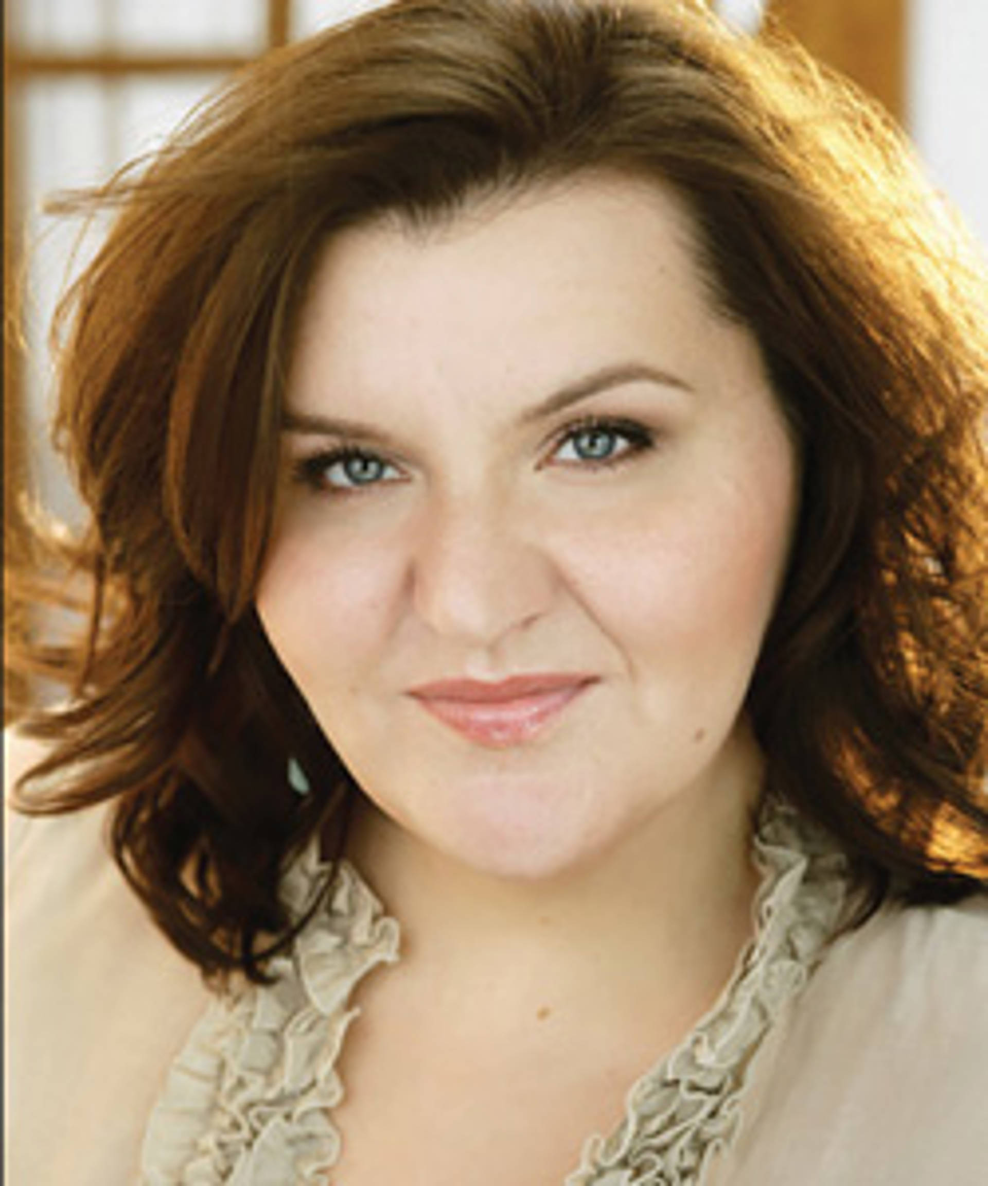 a white woman with brown hair and light eyes in a beige top.