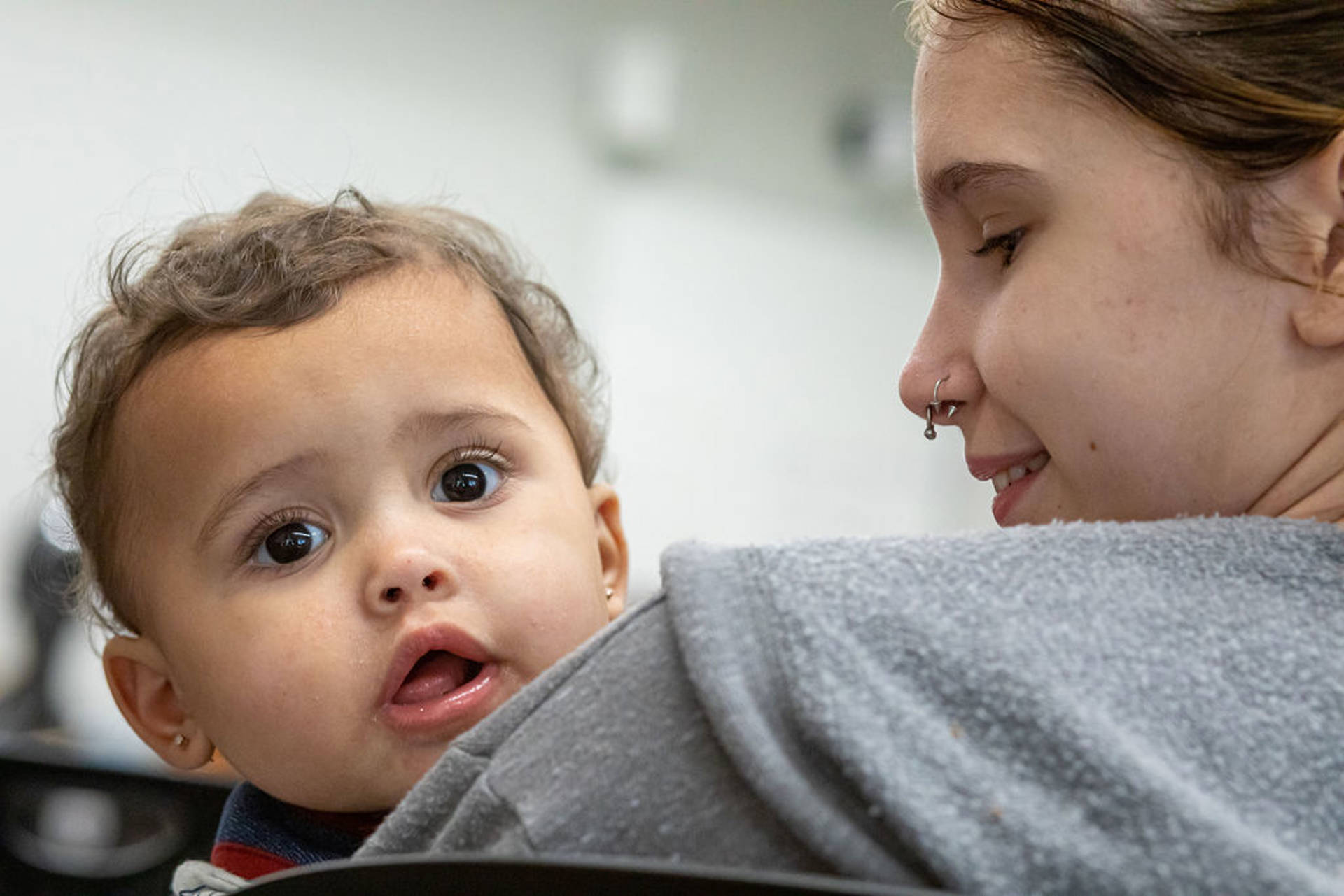 Closeup of a woman with light complexion and a nose ring smiling towards the infant held in her arms.