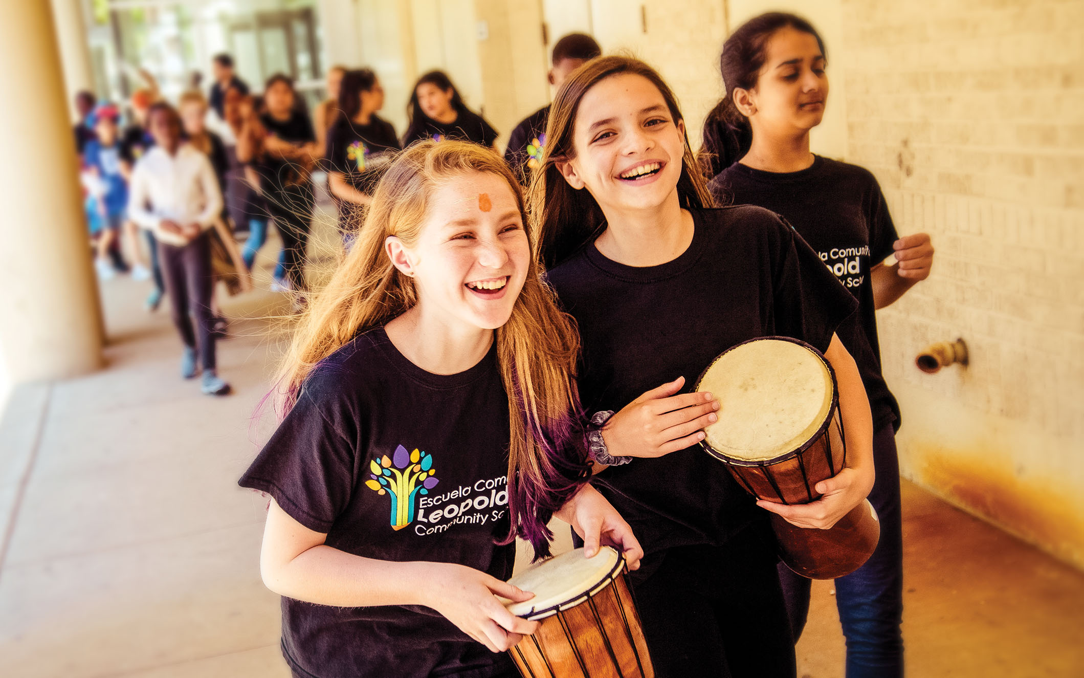 Two girls laugh and play drums as they walk alongside Overture Center.