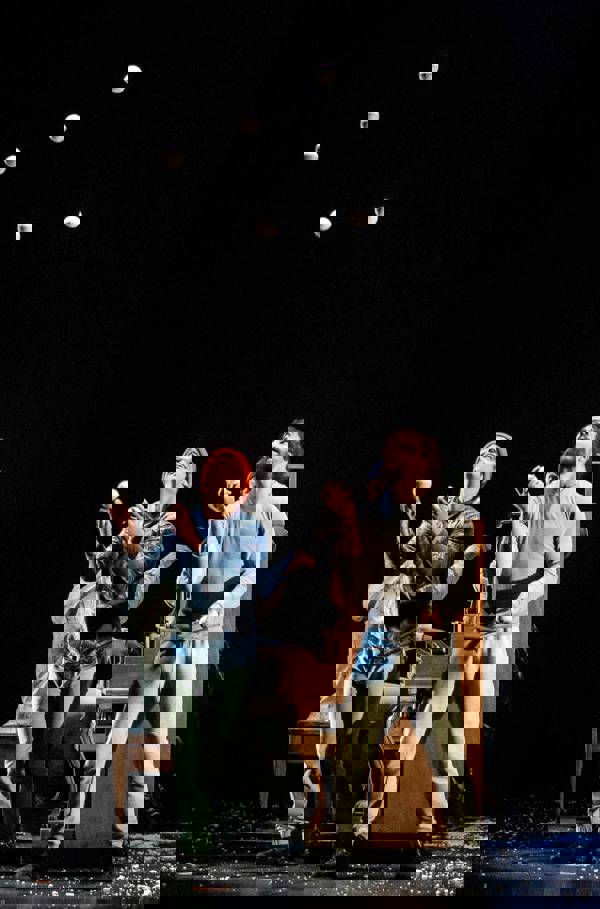 Two performers juggling six snowballs on stage with a piano player behind them.