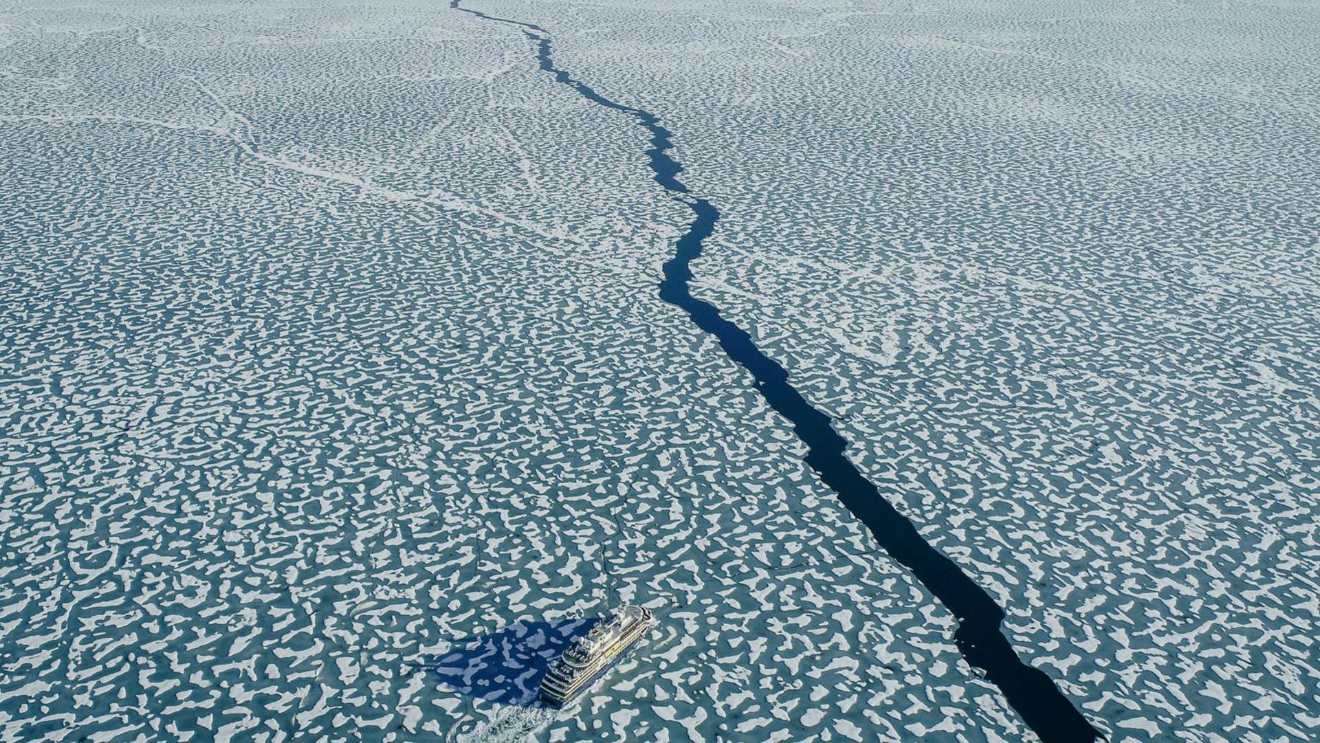 Arial shot of arctic waters with a ship passing through.