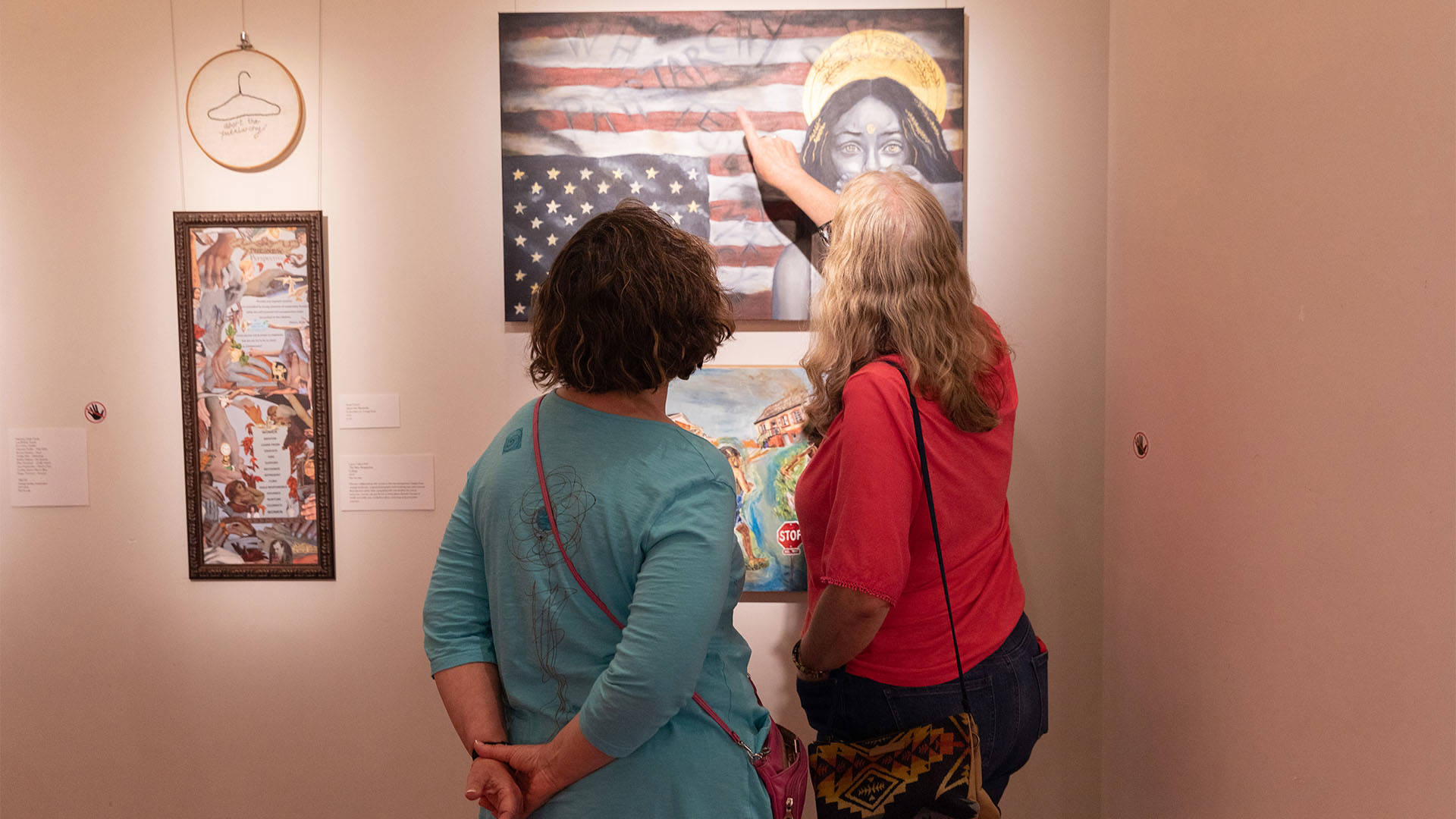 Two women look at a piece of art on a wall.