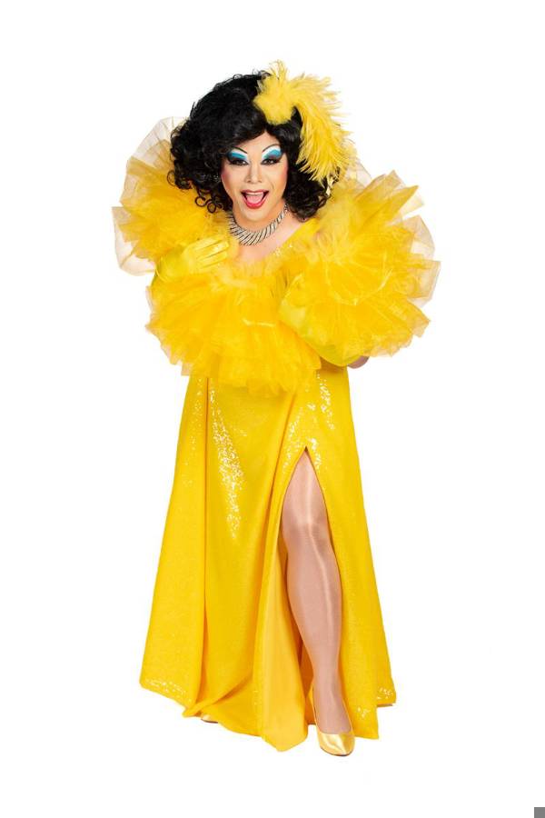 A drag performer with dark hair, colorful blue eye makeup and a bright yellow dress striking a dramatic pose.