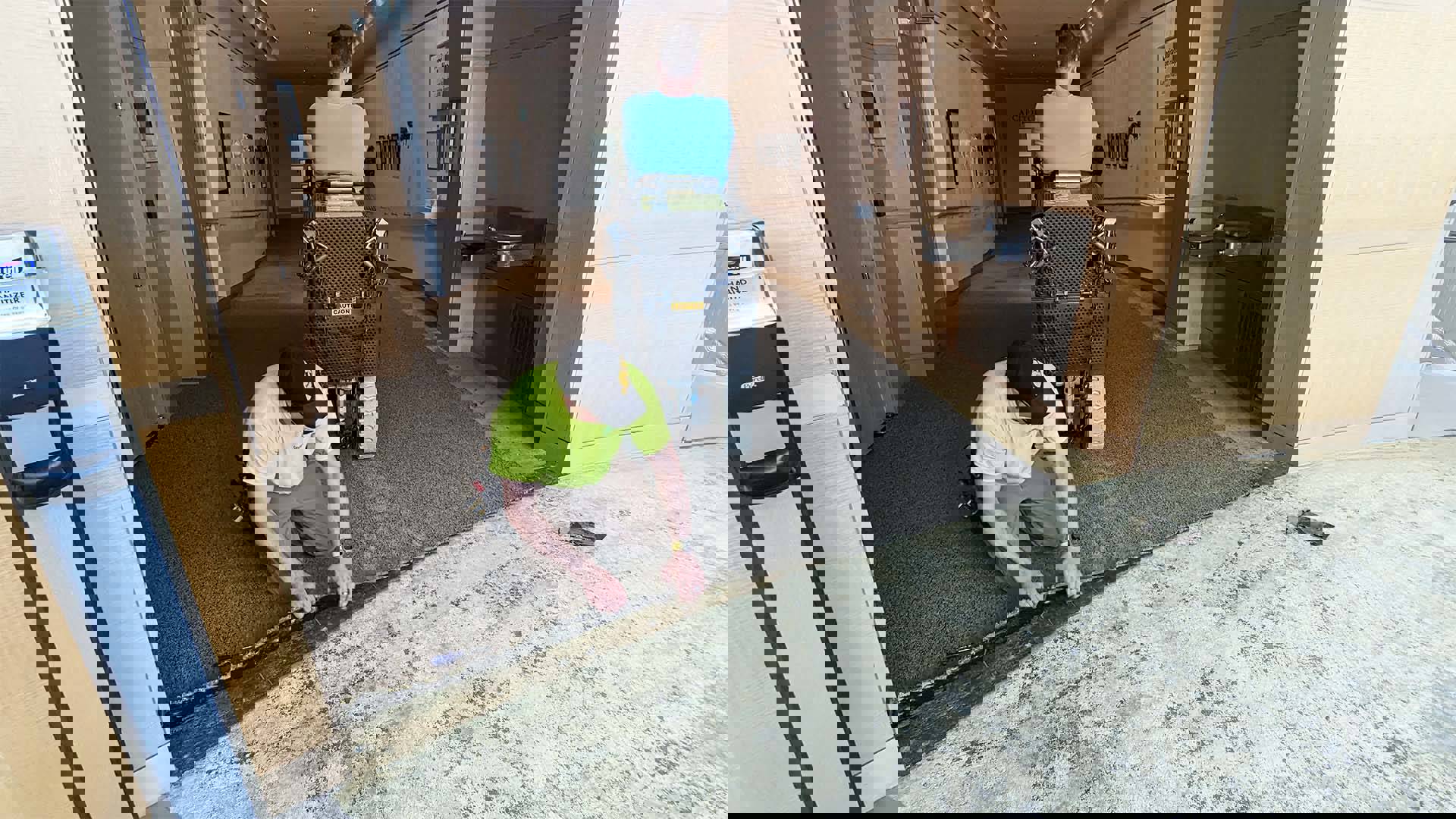 Two men pulling up carpeting in a beige hallway.