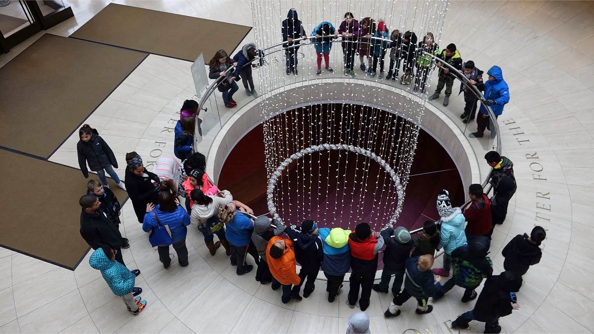 A group of kids standing in Overture's lobby. They are circled around an opening in the floor that looks down into the lower level.