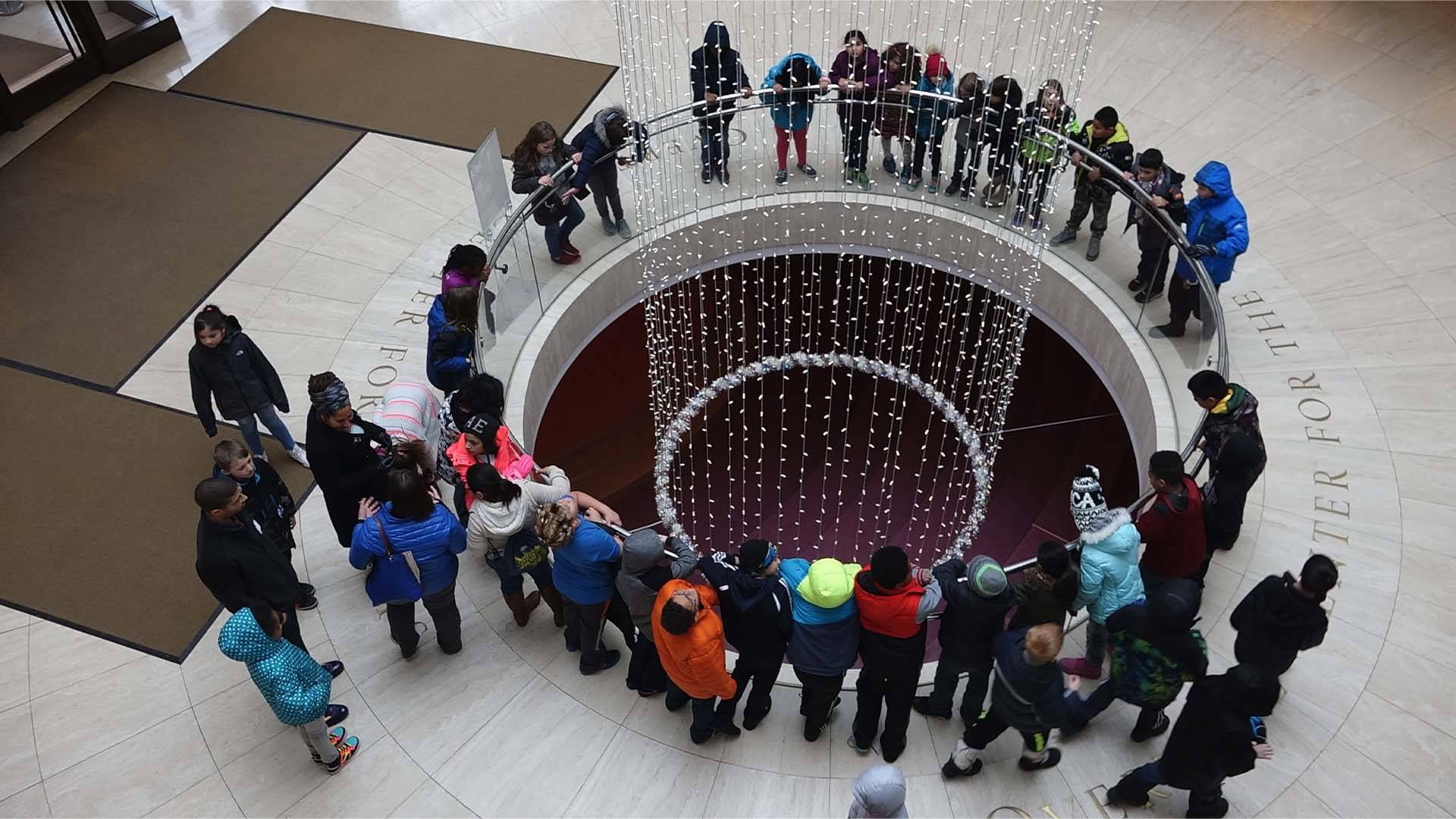 A group of kids standing in Overture's lobby. They are circled around an opening in the floor that looks down into the lower level.