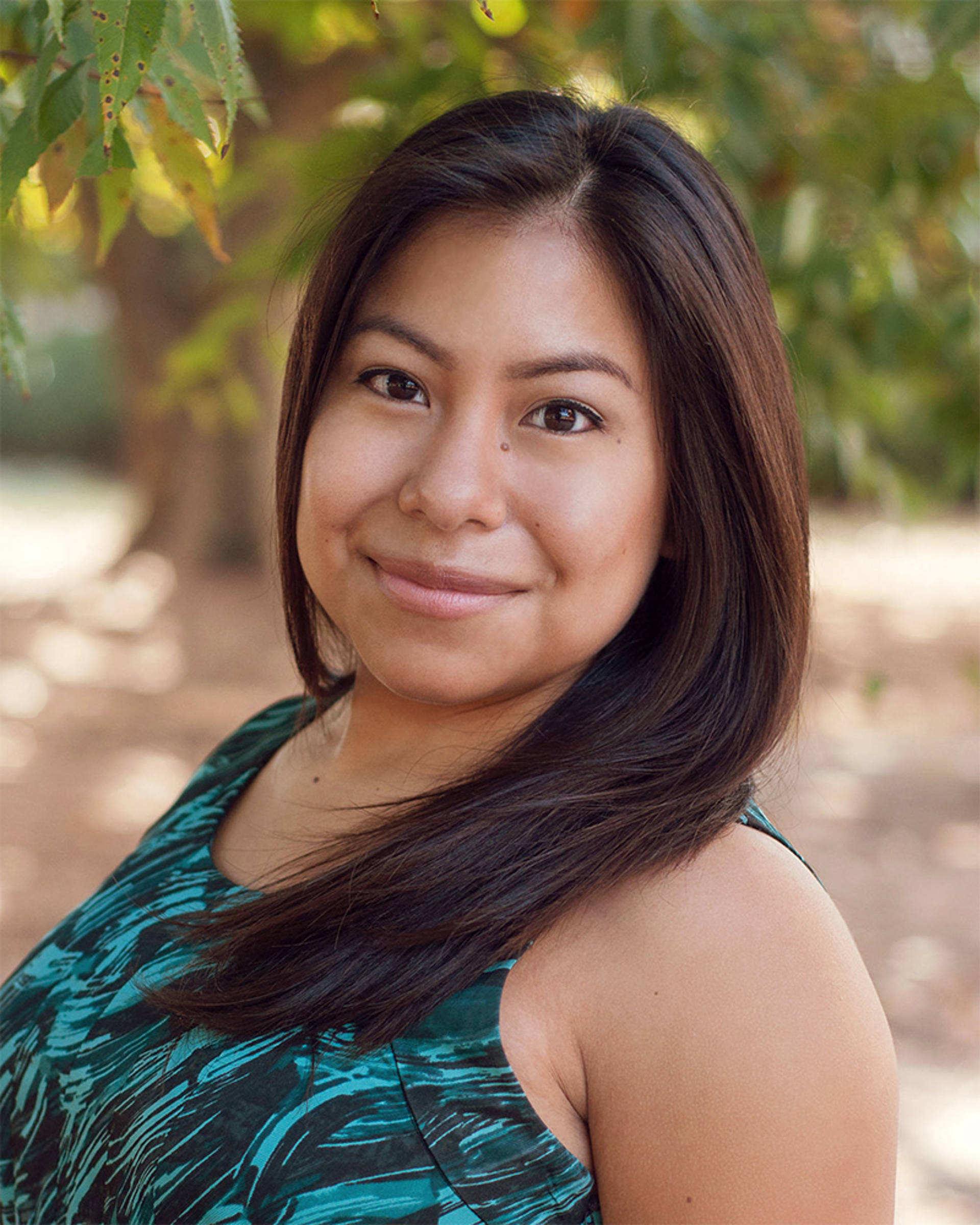 Headshot of a woman with medium complexion, dark hair, dark eyes and a teal top.