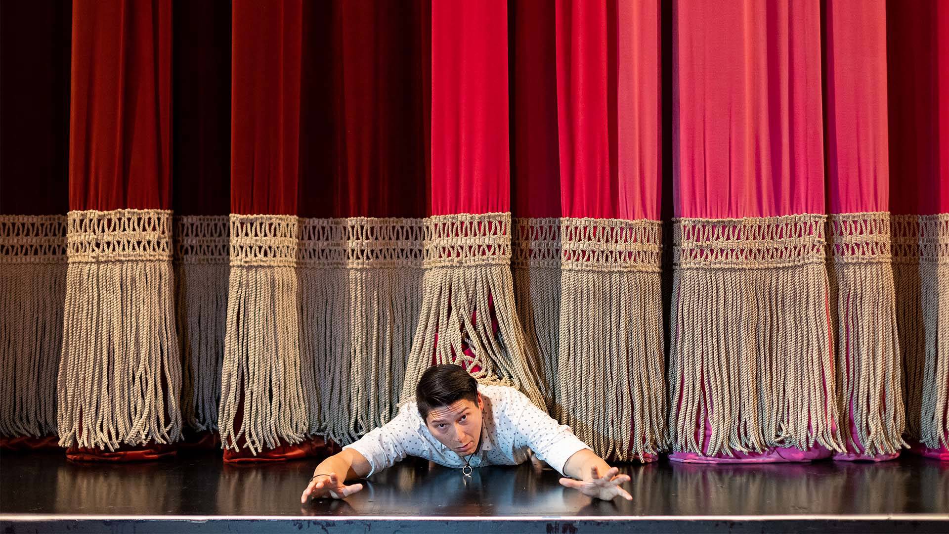 A person stuck under a red stage curtain. He is reaching out for help.