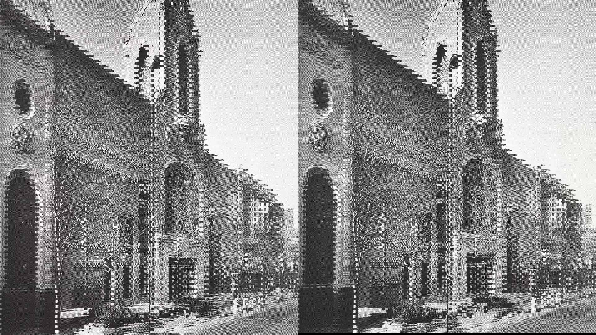 Greyscale shot of the old civic center facade. With ornate brick and arched designs. There is alsoa a sidewalk and several trees missing their leaves.