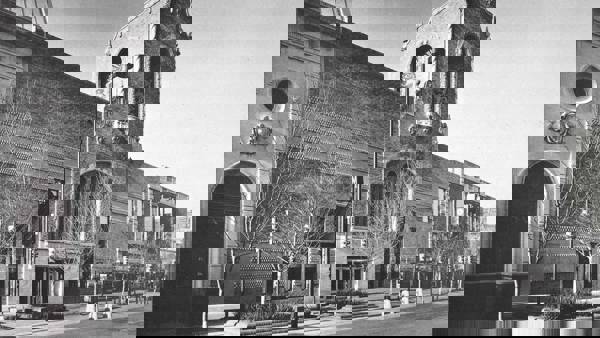 Greyscale shot of the old civic center facade. With ornate brick and arched designs. There is alsoa a sidewalk and several trees missing their leaves.