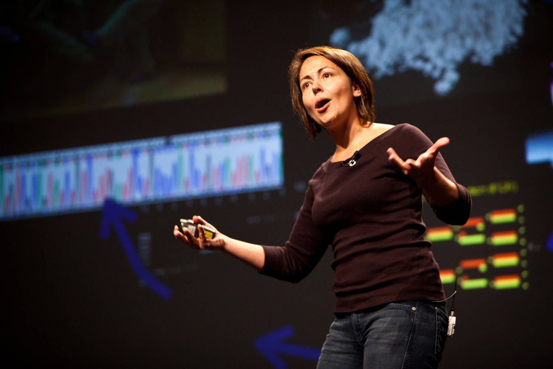 Beth Shapiro giving a lecture. She is a white woman with shoulder length brown hair wearing a black t-shirt.