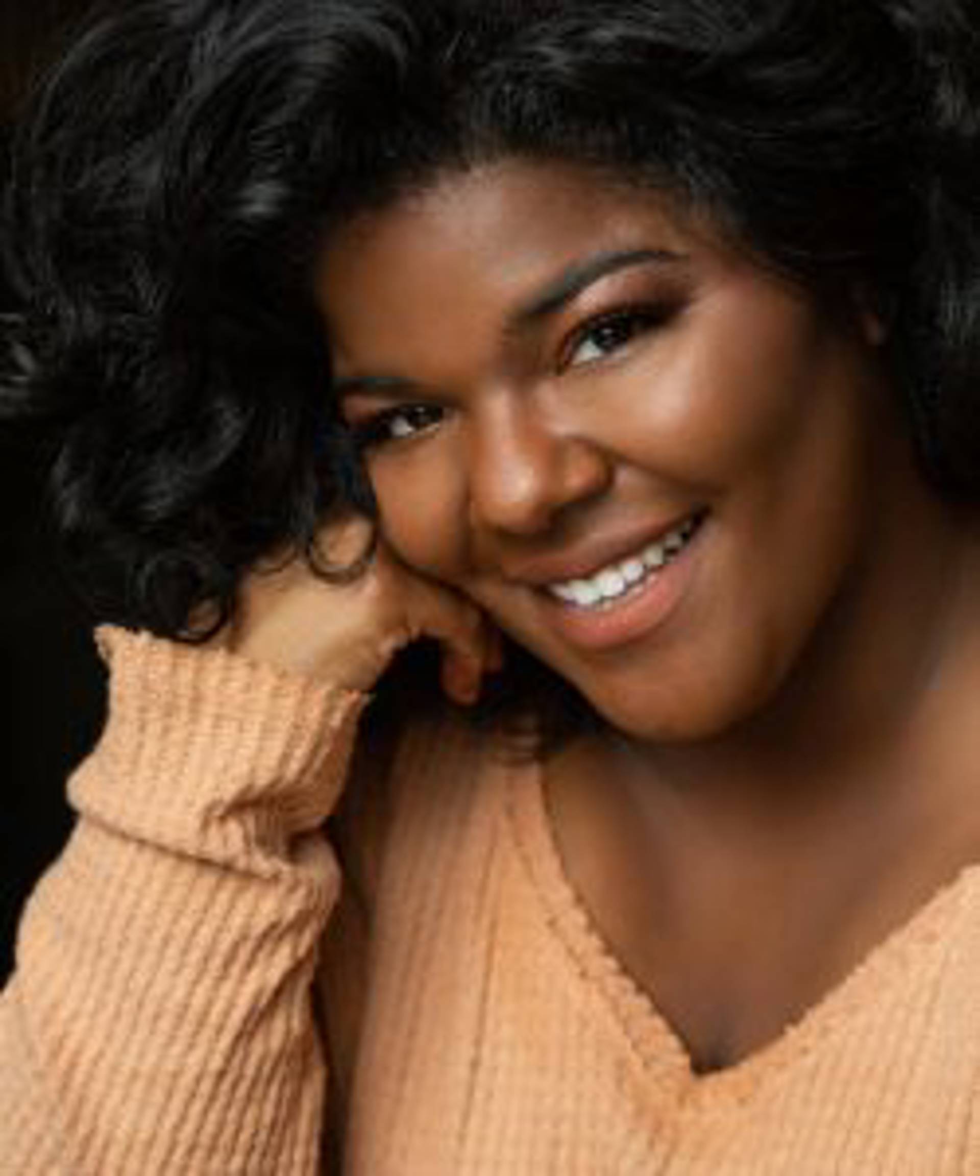Headshot of an African American woman with brown eyes and wavy hair in a light orange top.
