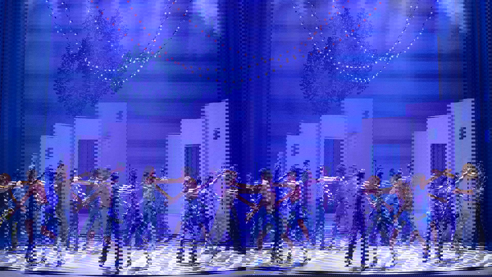 The Mamma Mia ensemble dancing in pairs against a blue background.