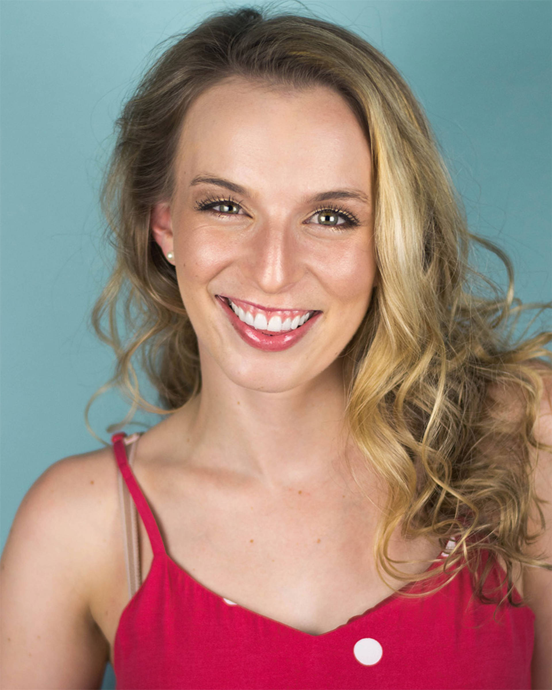Headshot of a woman with light complexion, hazel eyes, blond hair and a red top.