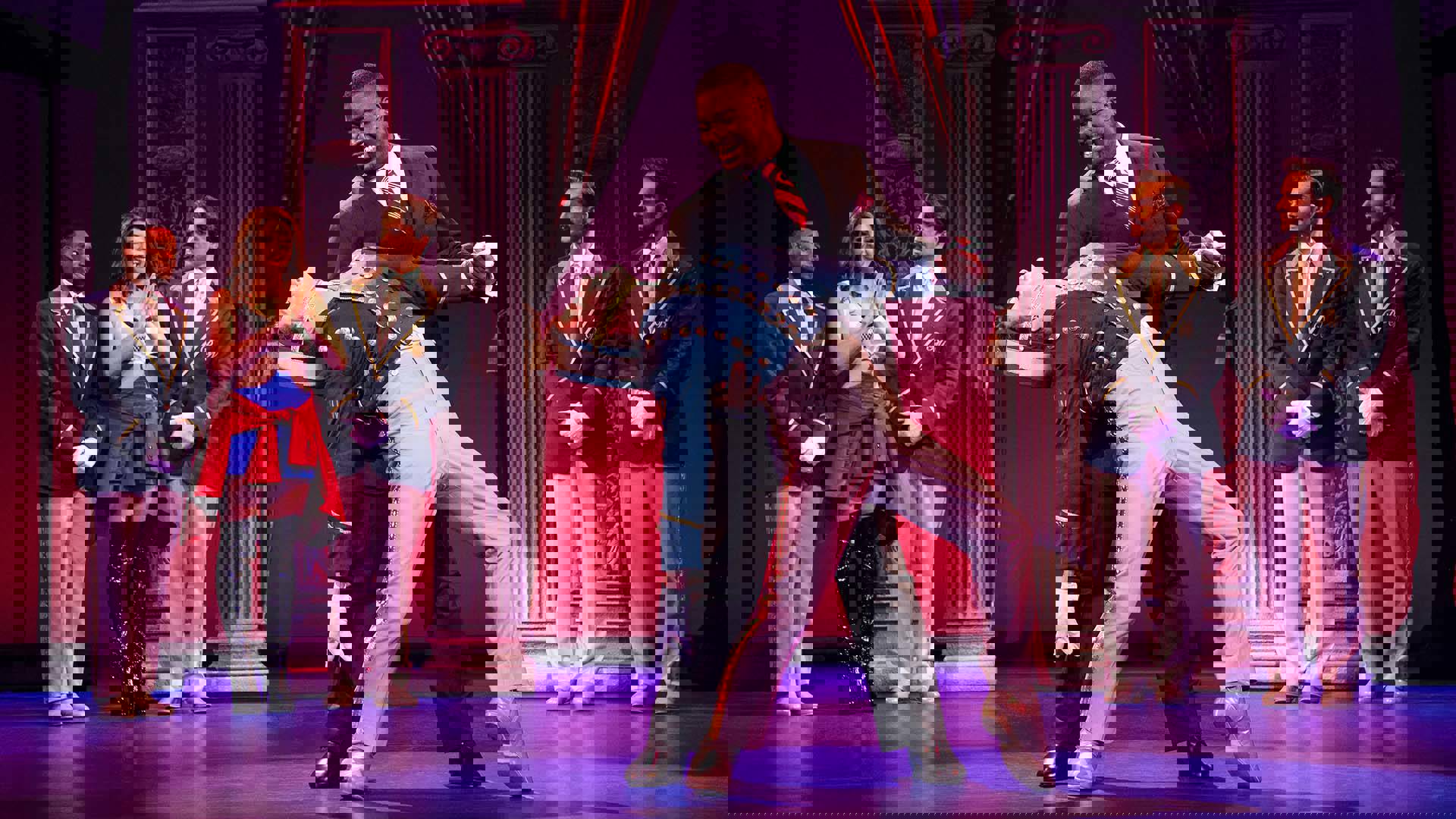 Two men - one in a suit and the other in a bellhop uniform, dance on a stage.