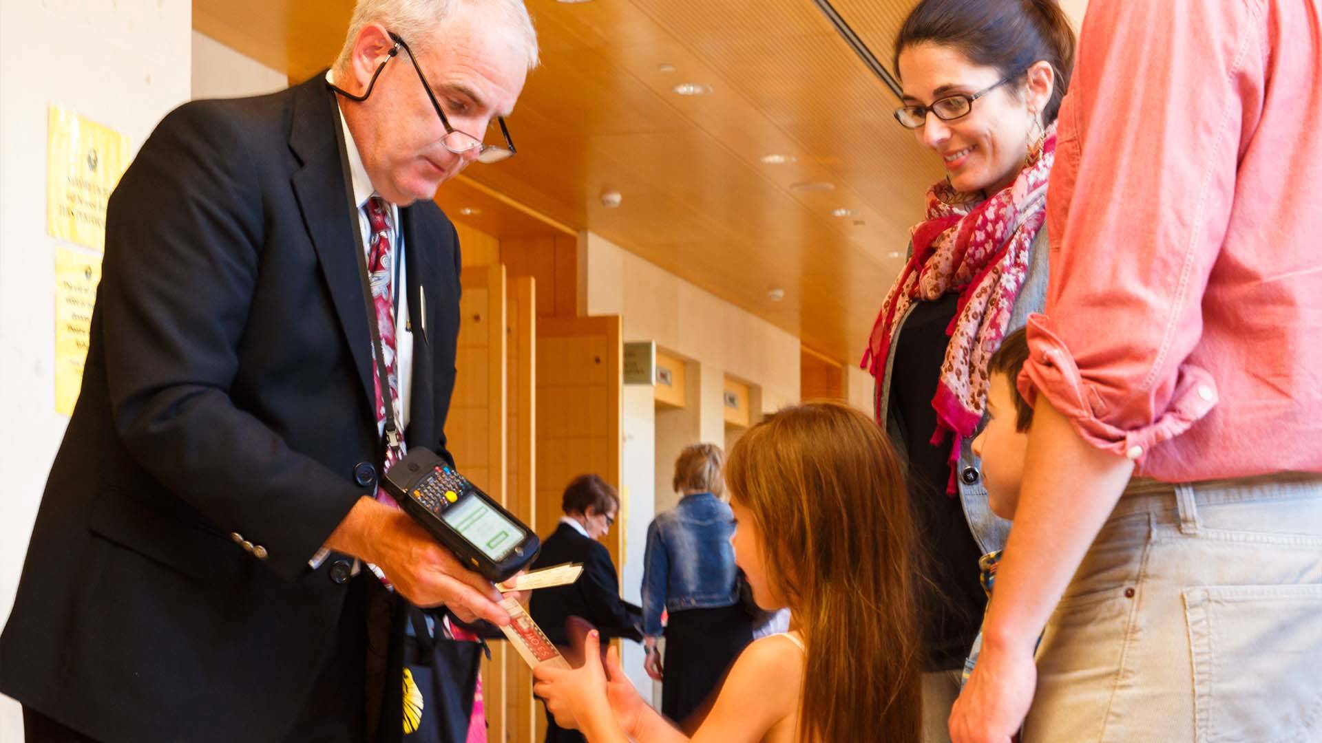 A white man in a suit scanning a child's ticket.