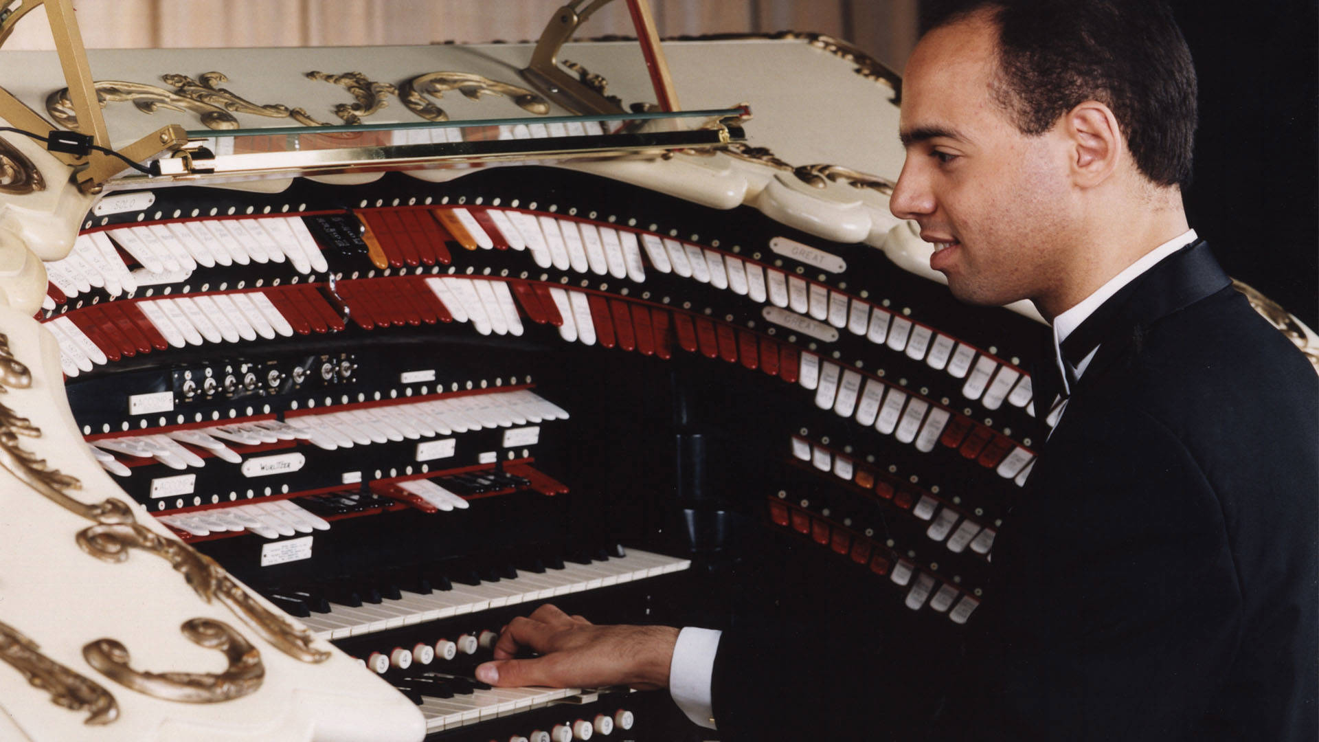 a young caucasian man in a tux playing an organ console.
