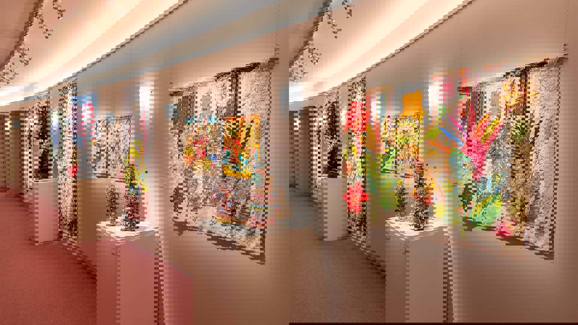 Playhouse Gallery's exhibit Garbology. Multiple colorful and floral tapestries on a white curved wall, three wire and multi-material sculptures on a white pedestal.