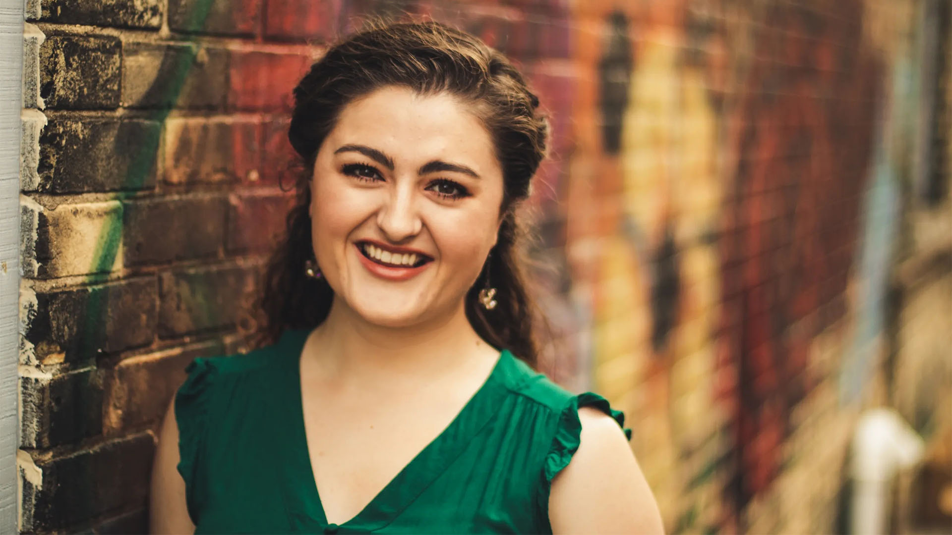 A smiling young caucasian woman with long brown hair and brown eyes wearing a green top.