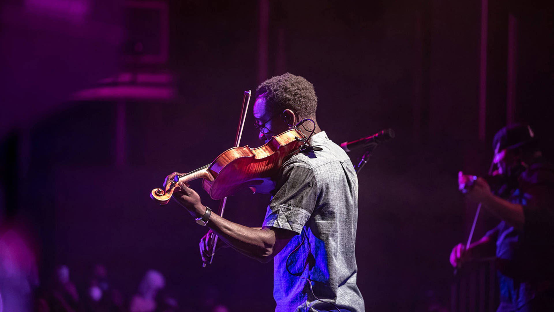 Wil Baptiste facing the audience on stage. He is playing the violin.