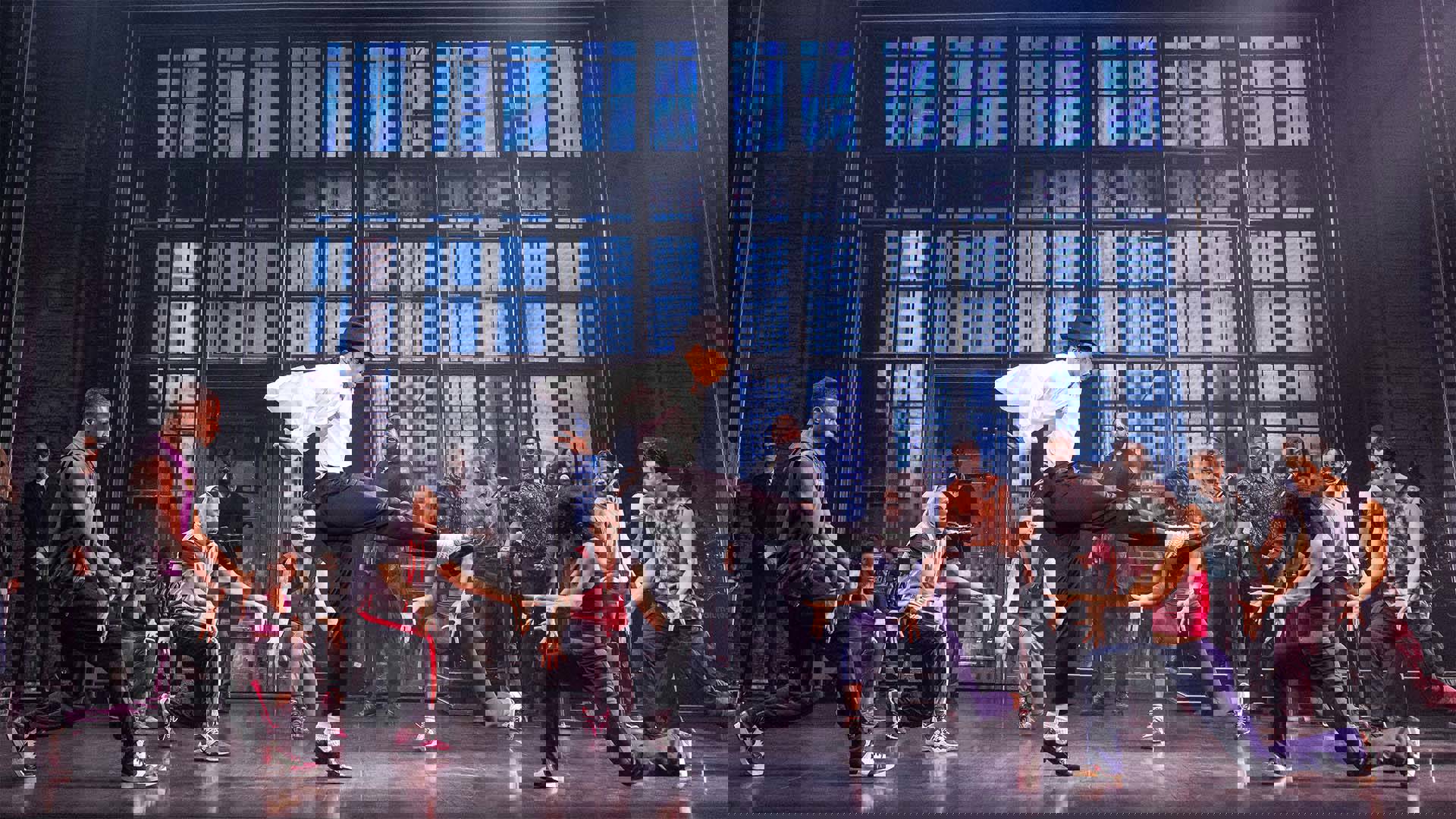 An actor playing Michael Jackson dancing on stage. He has medium complexion, dark hair, a white shirt, and dark pants. There are other actors facing him.