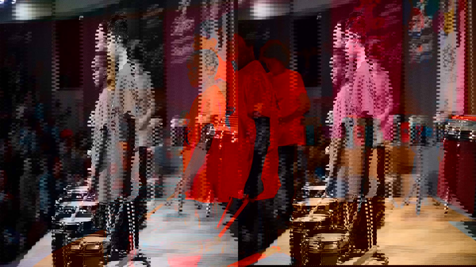 Four young people in bright orange t-shirts performing on Rotunda Stage with drums and mallets.