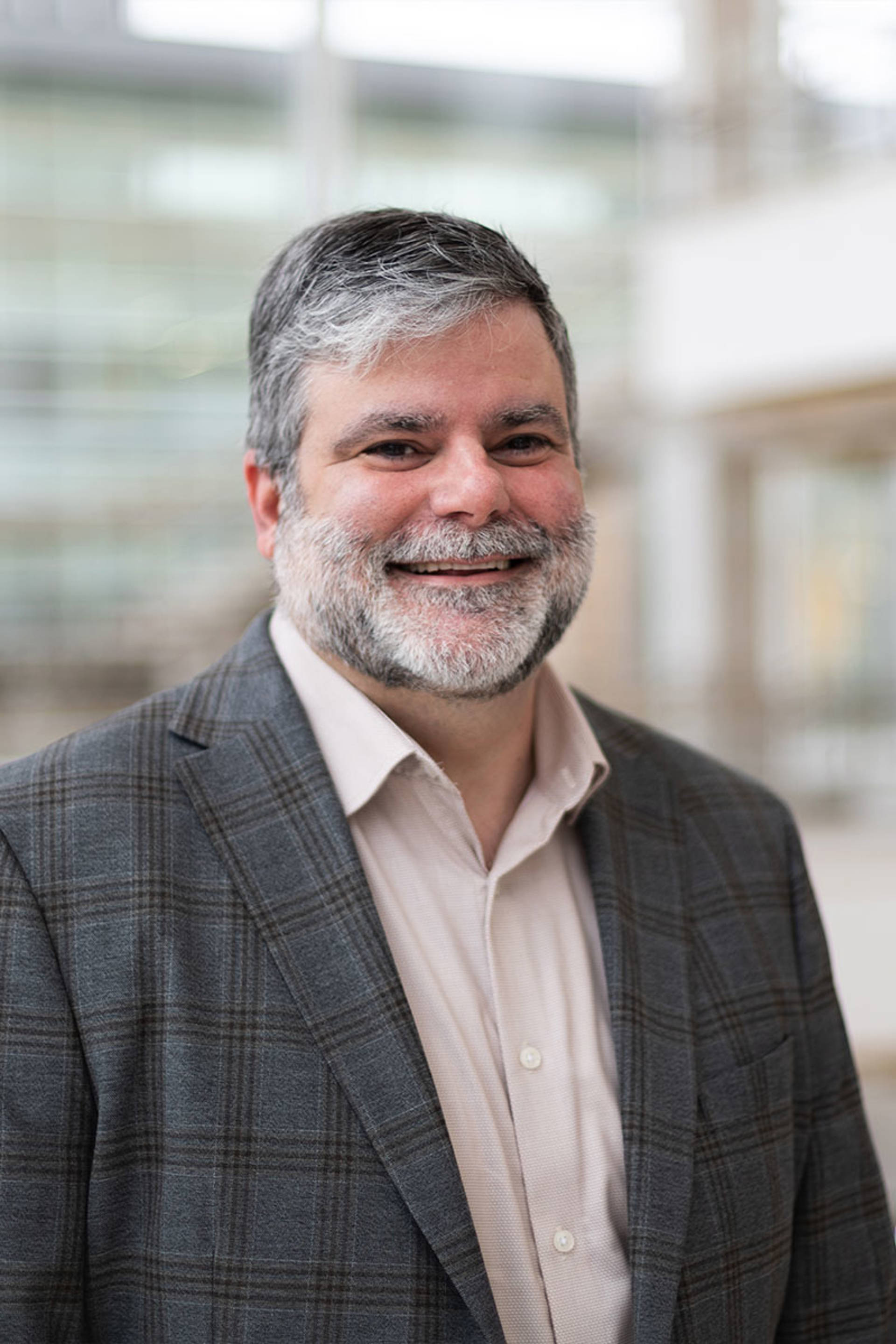 Mike Conway headshot. A middle aged caucasian man with greying short hair and a grey-white beard. He is smiling and wearing a grey suit jacket and white button up shirt.