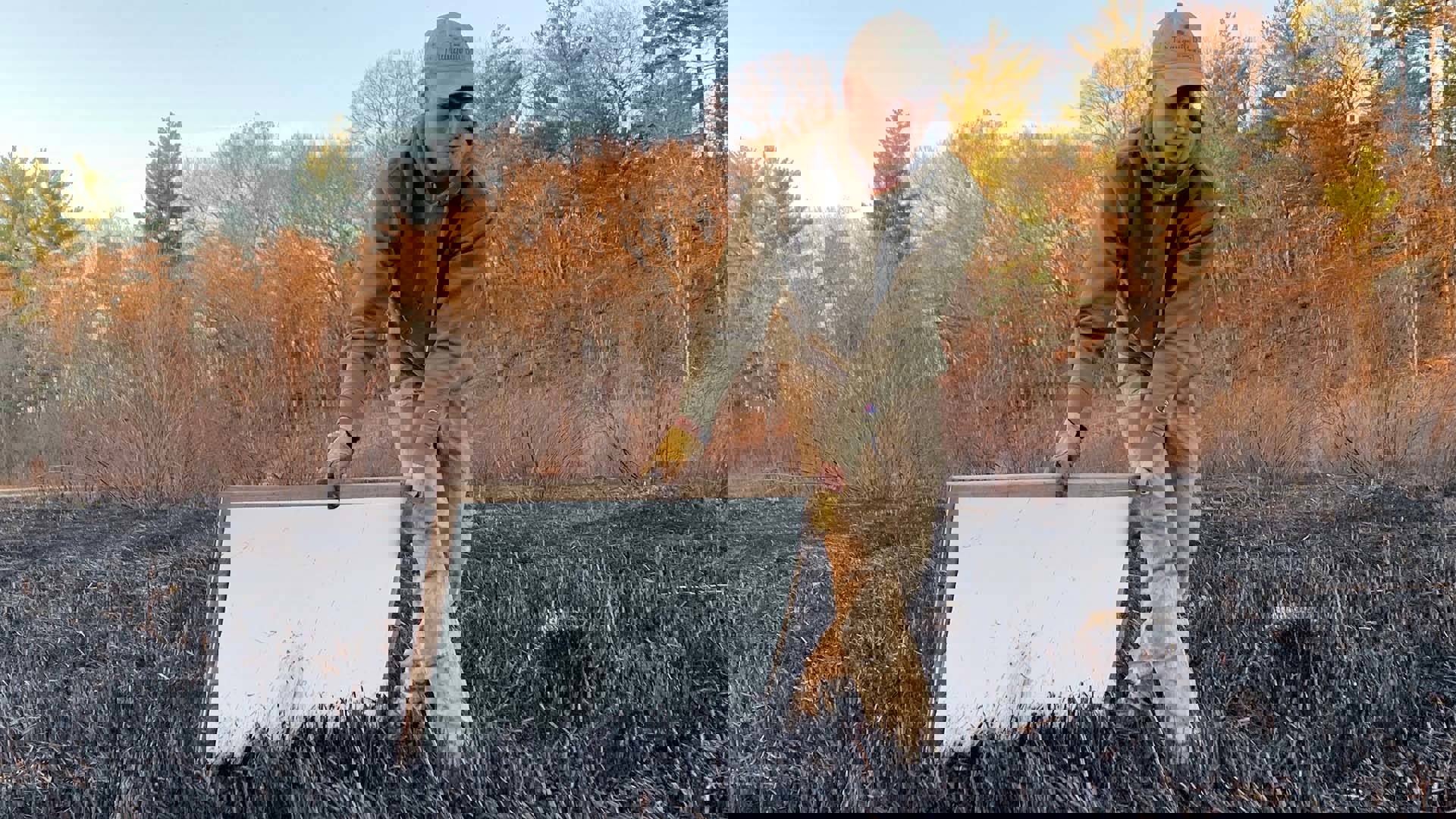 A man with light complexion, a baseball hat and a hoody pushing a canvas through field that was recently part of a controlled burn.