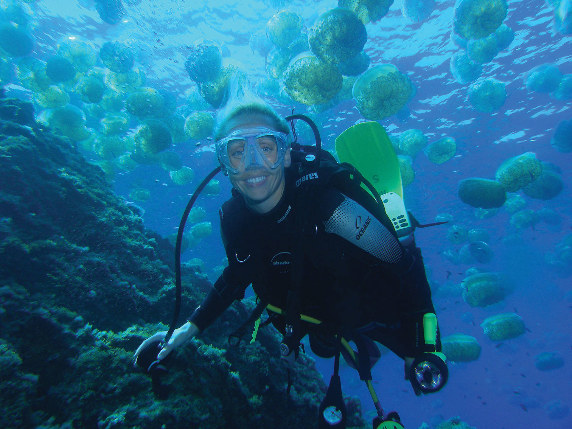Lucy Hawkes underwater surrounded by fish in scuba gear smiling towards the camera