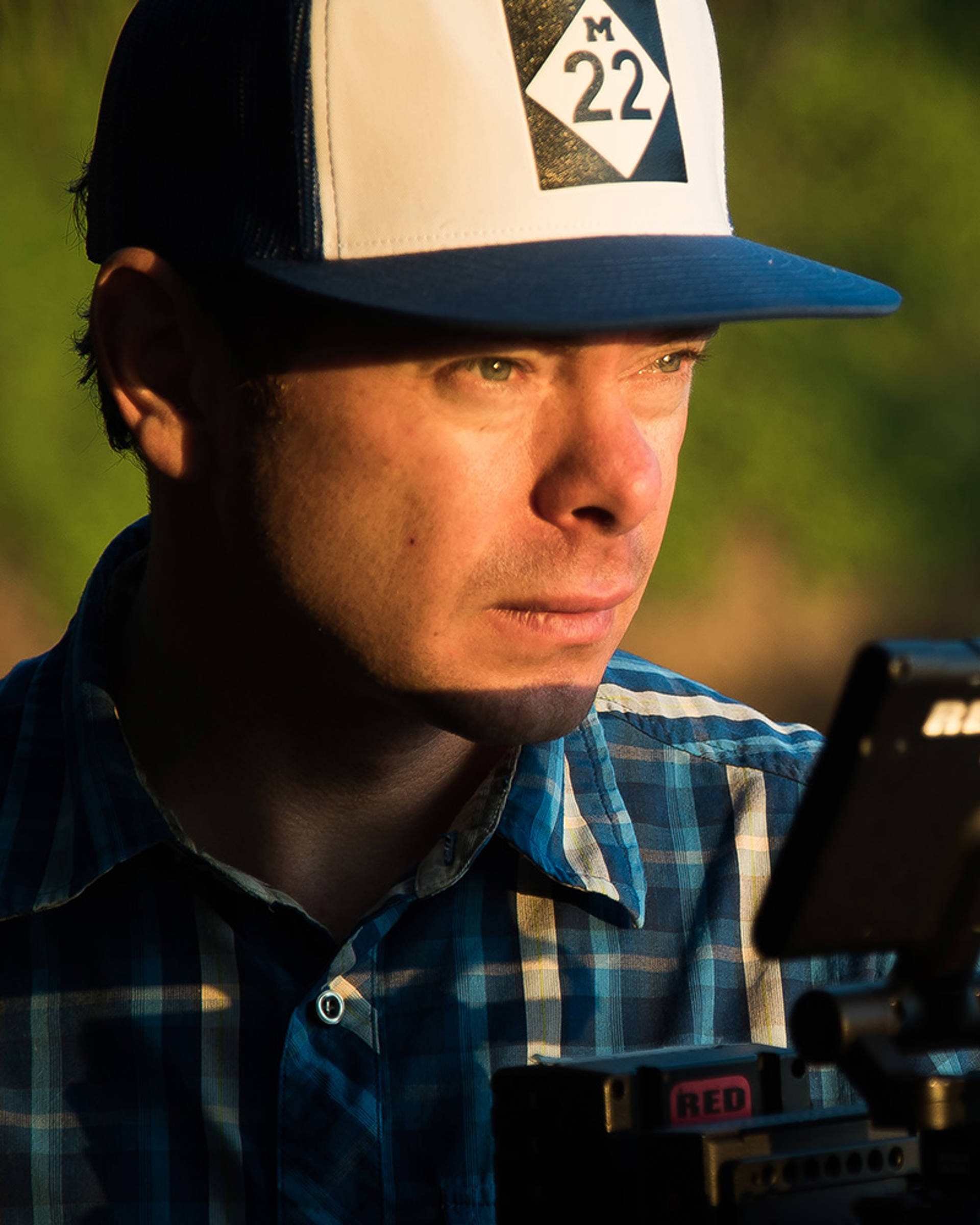 A caucasian man with a blue eyes and a baseball cap and a plaid shirt on