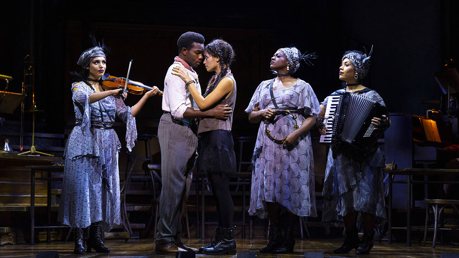 A young African American woman and man embrace each other. Behind them, three musicians are facing inward.
