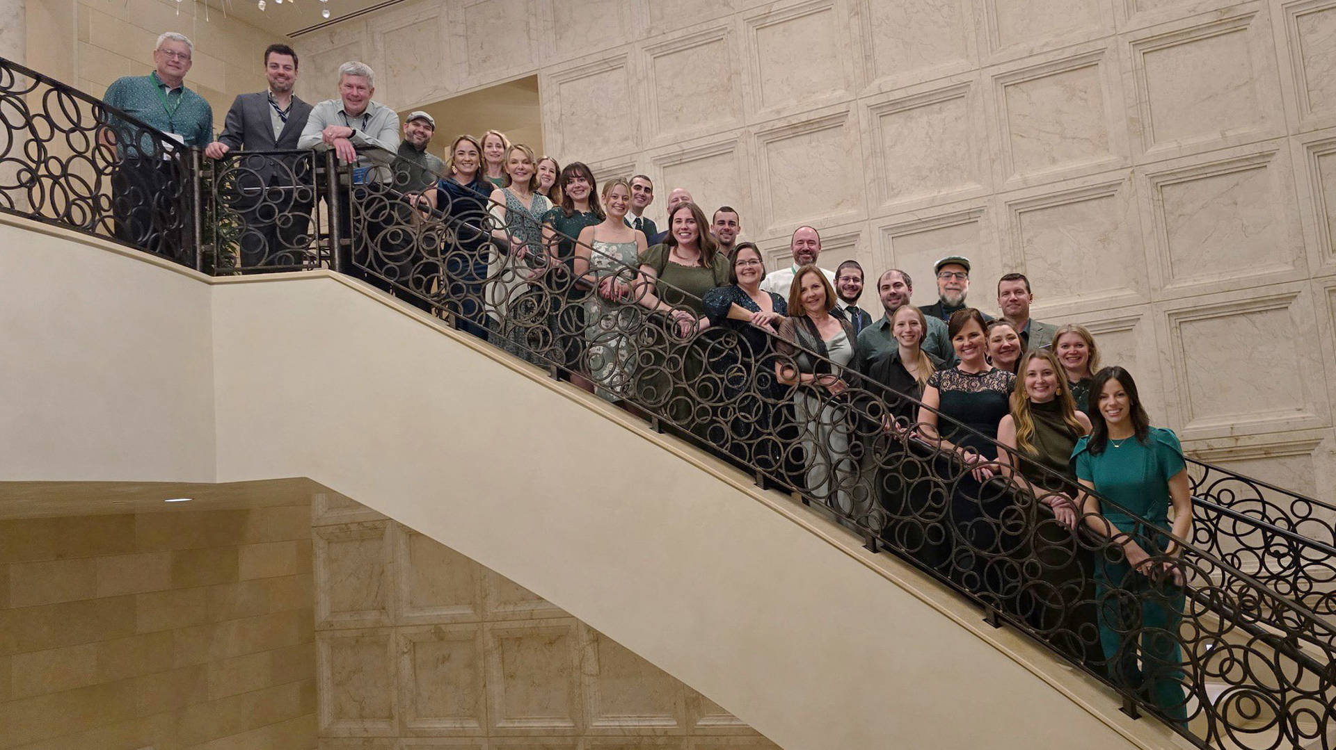 A group of smiling people standing together on a staircase for a photo.