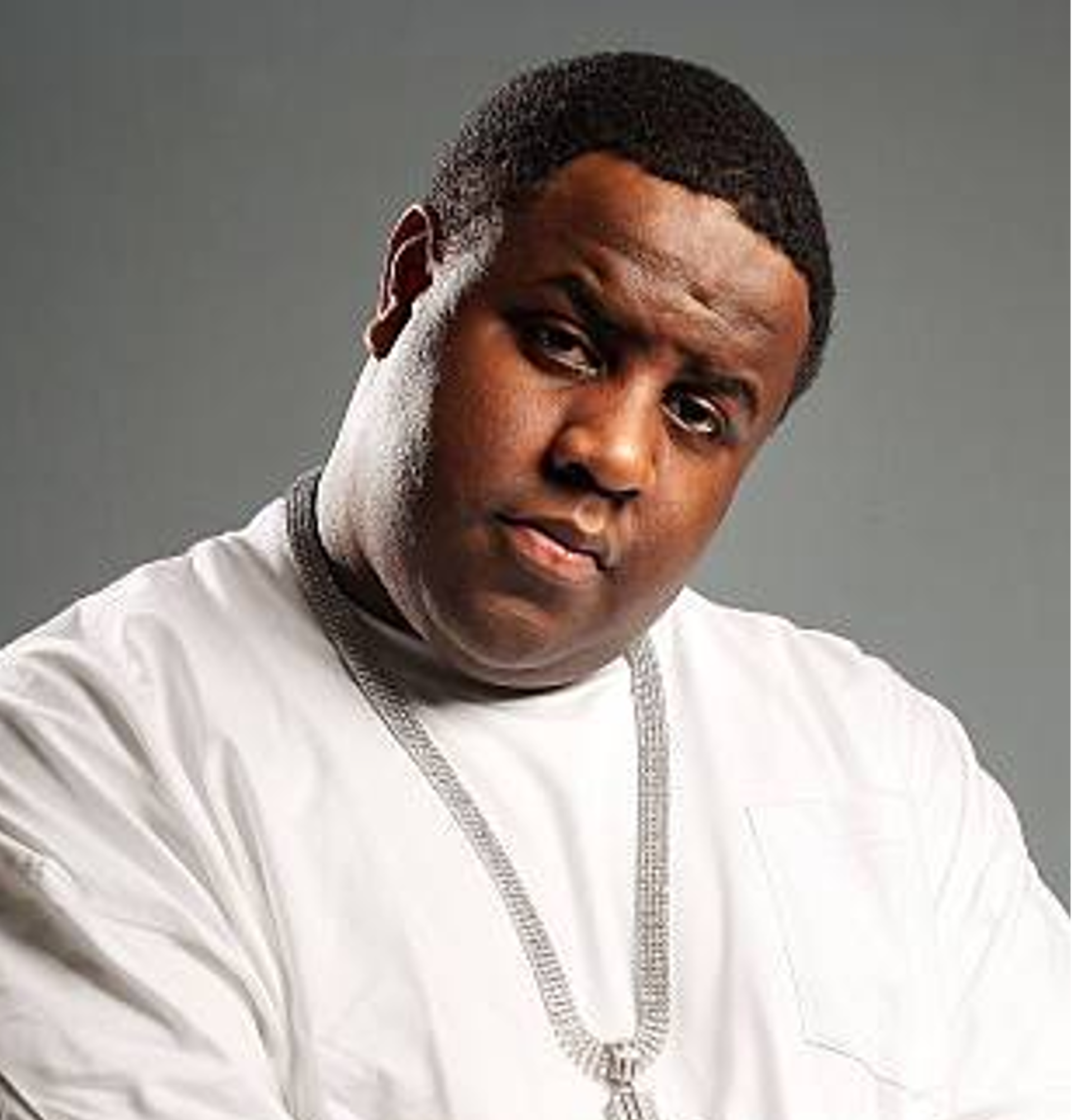 Headshot of young african american man with short dark hair brown eyes and white top. He is tilting his head to his left.