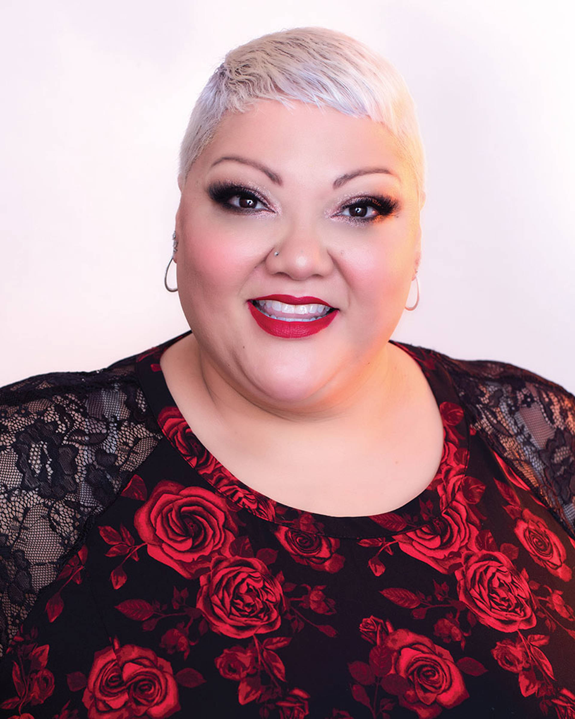 Headshot of a woman with dark eyes, short white hair, and a flower pattern top.