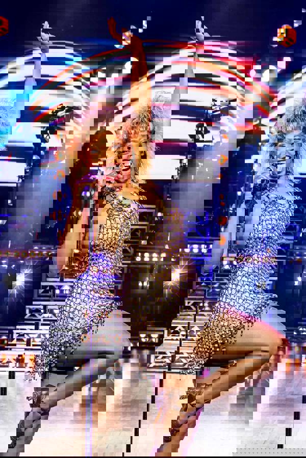 An African American woman in a gold dress singing into a handheld microphone lifting her right knee up.