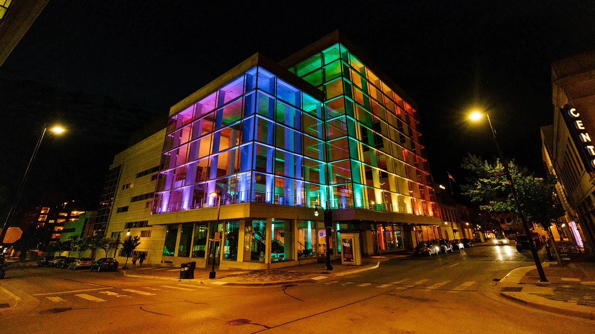 Overture Center glass exterior, lit up with a rainbow of multiple colors, at night time.