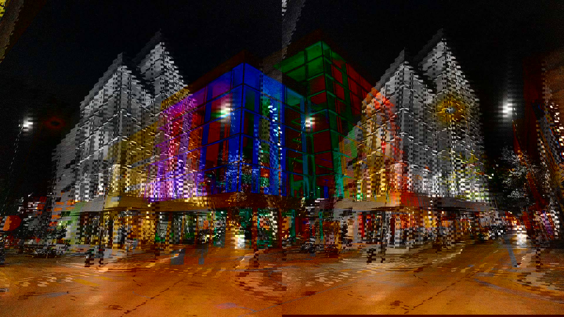Overture Center glass exterior, lit up with a rainbow of multiple colors, at night time.