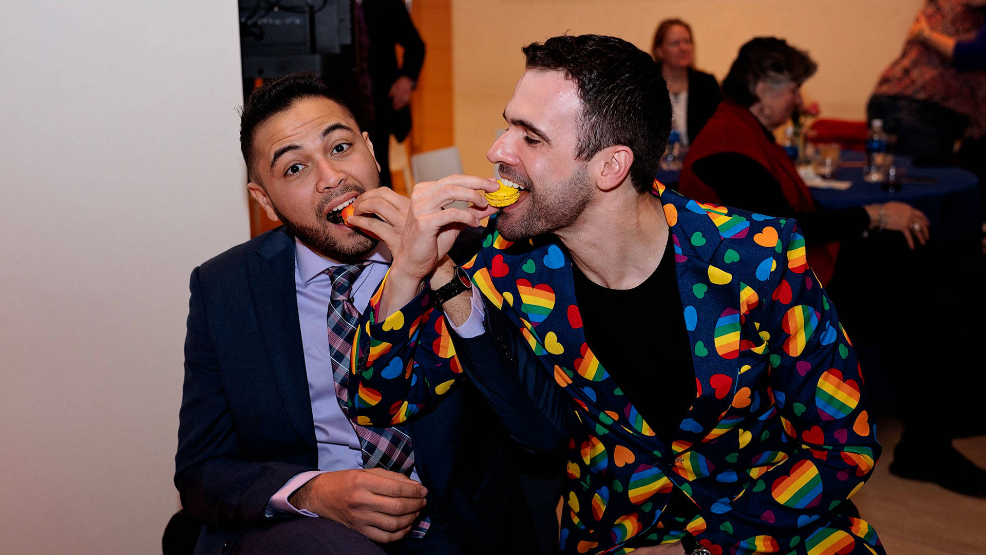 Two men eating macaroons and smiling together.