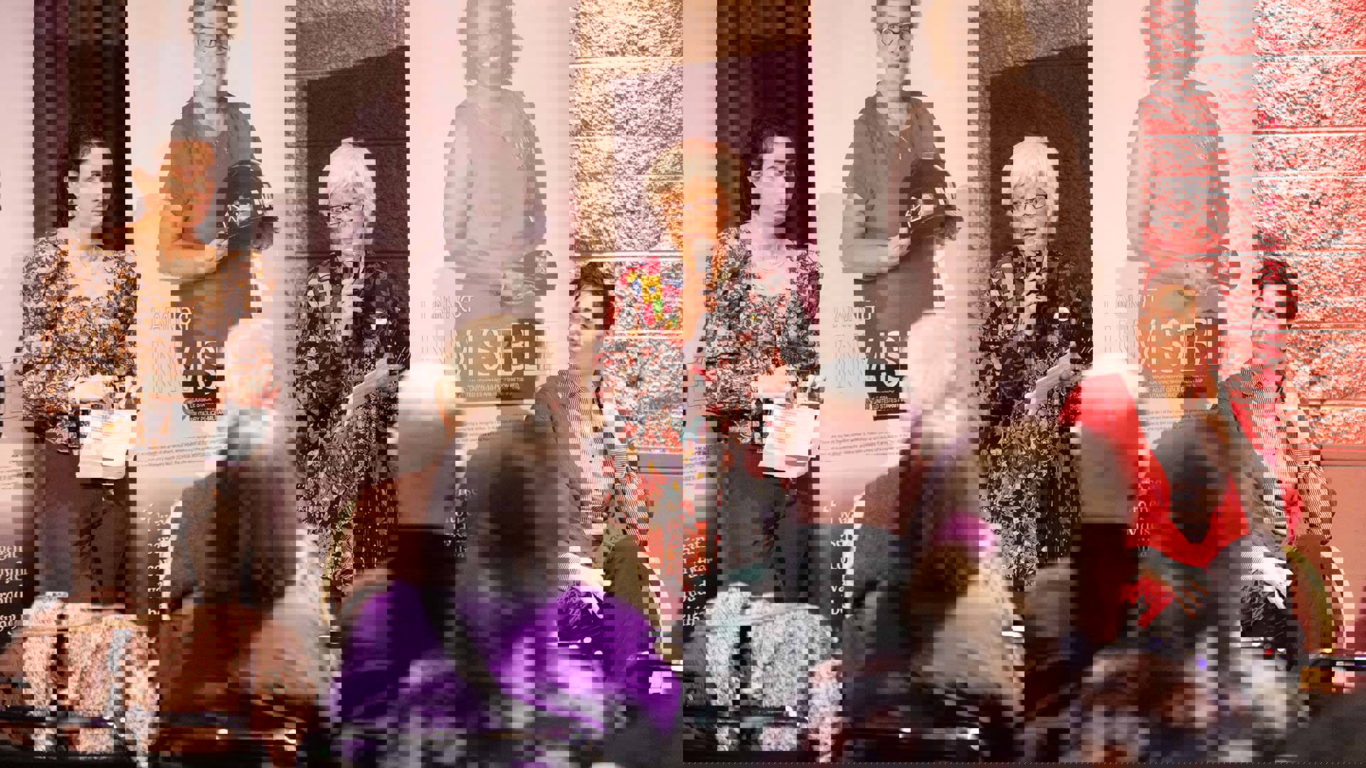 A woman with short white hair, medium complexion and a colorful top speaking into a microphone as others listen.