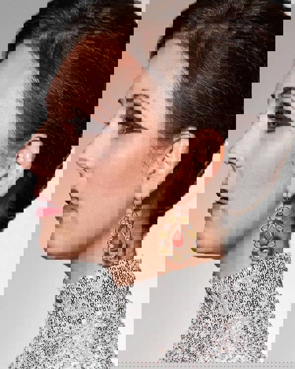 profile of a caucasian woman with blue eyes, dark hair, a grey turtleneck, and large earings. She has striking dark eye shadow.