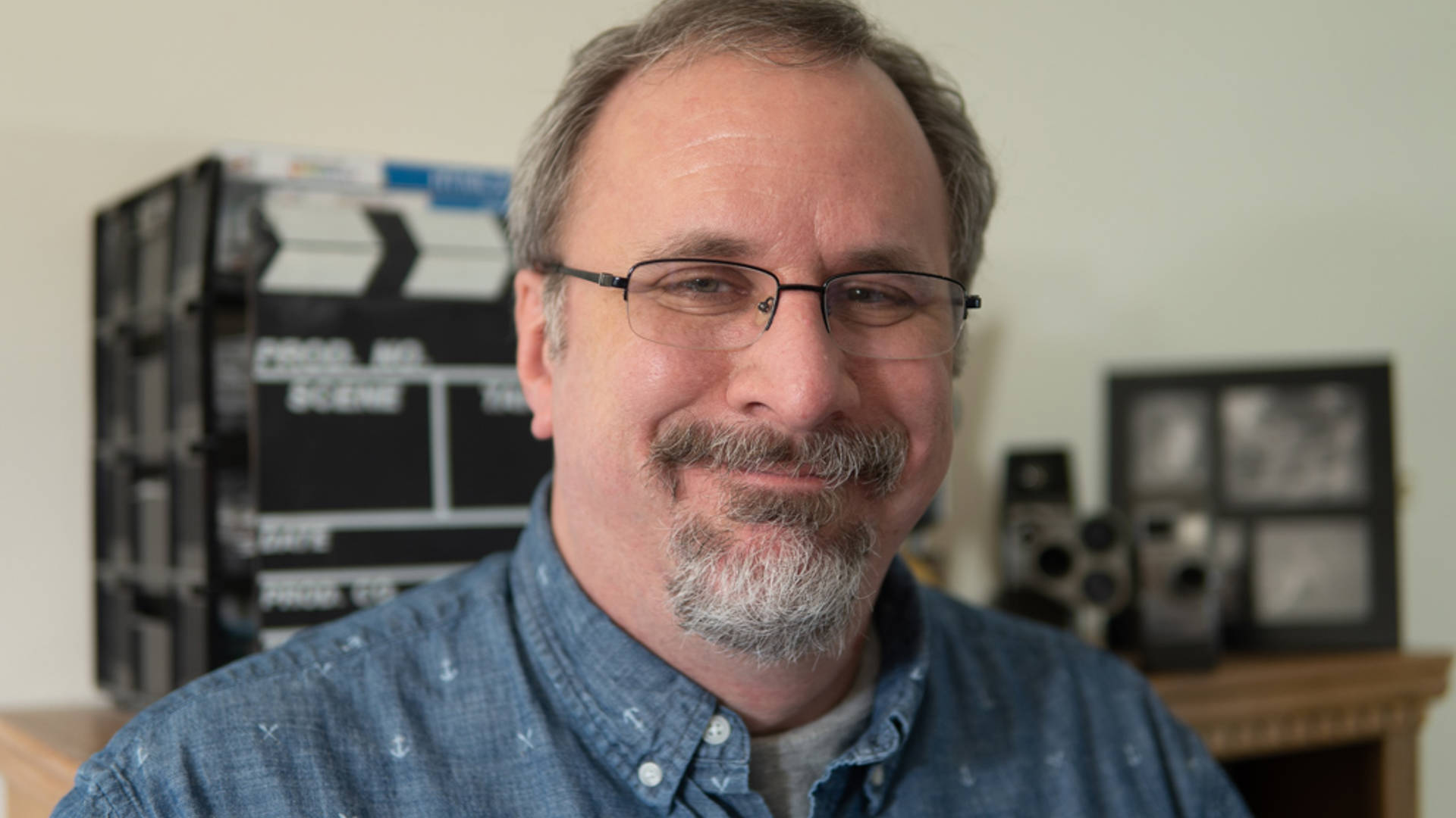 Headshots of a middleaged caucasian man. He has a goatee, grey hair, glasses, and a blue collared shirt.