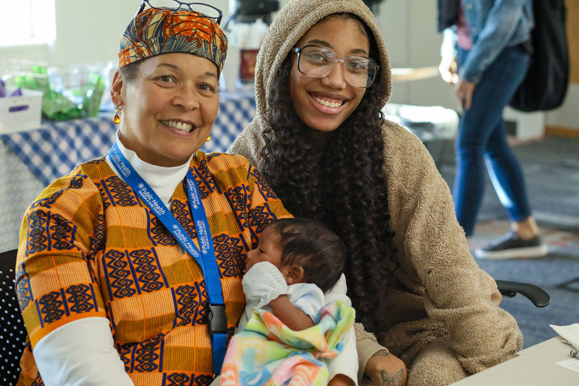 Two women with dark complexion and brown eyes sitting together for a photo with an infant.